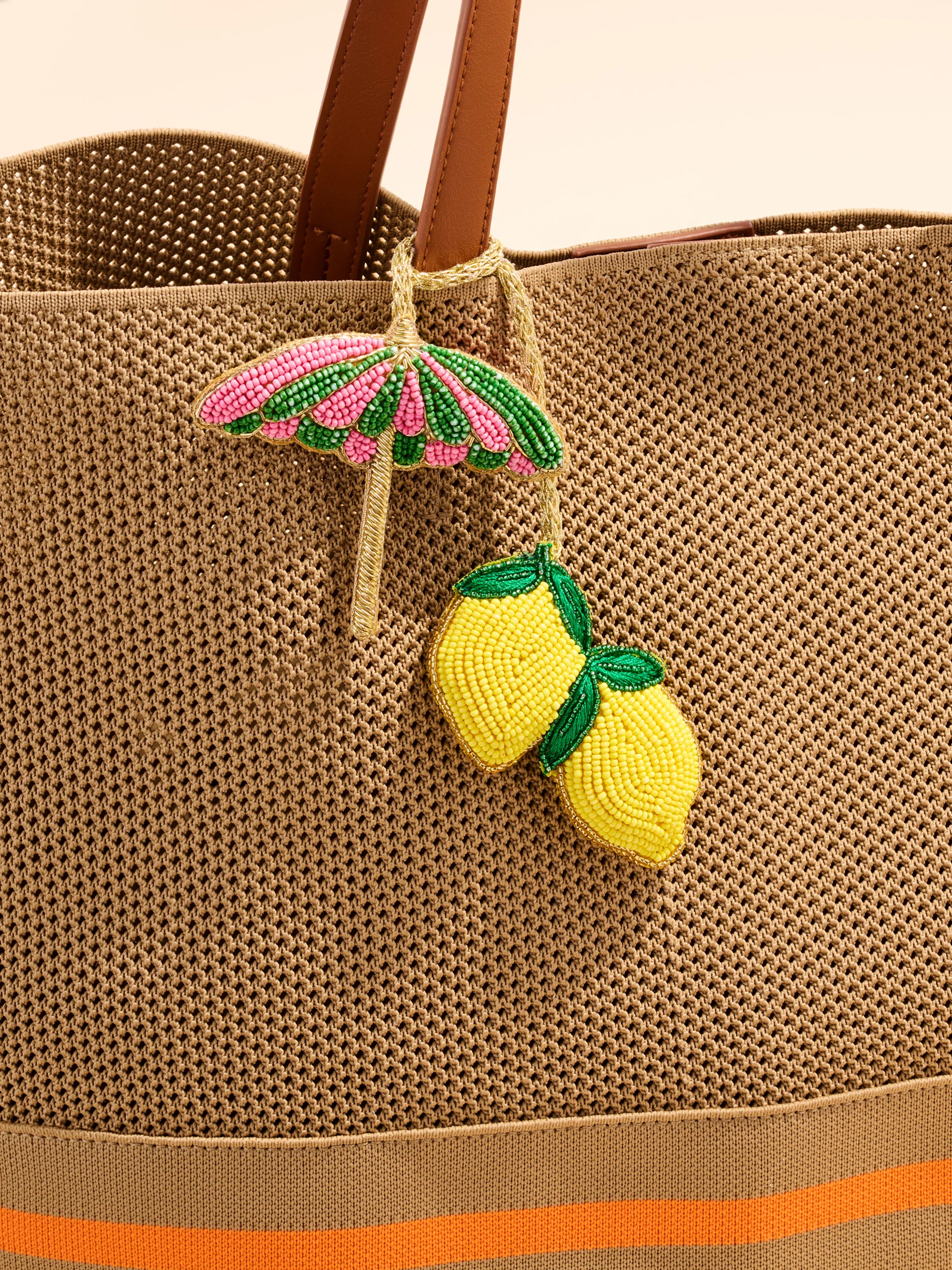 Brown textured bag with a pink umbrella and yellow lemon charm on a beige background