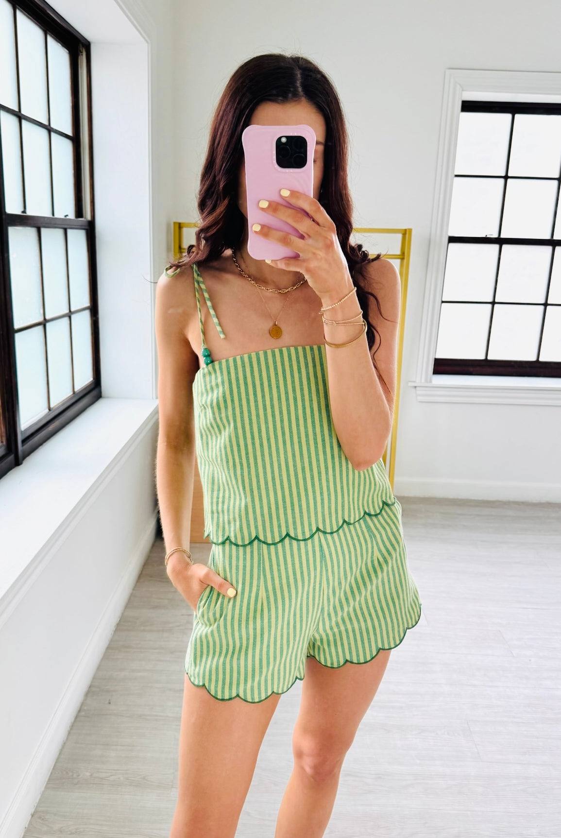 Woman taking a mirror selfie wearing a green and white striped dress in a bright room.