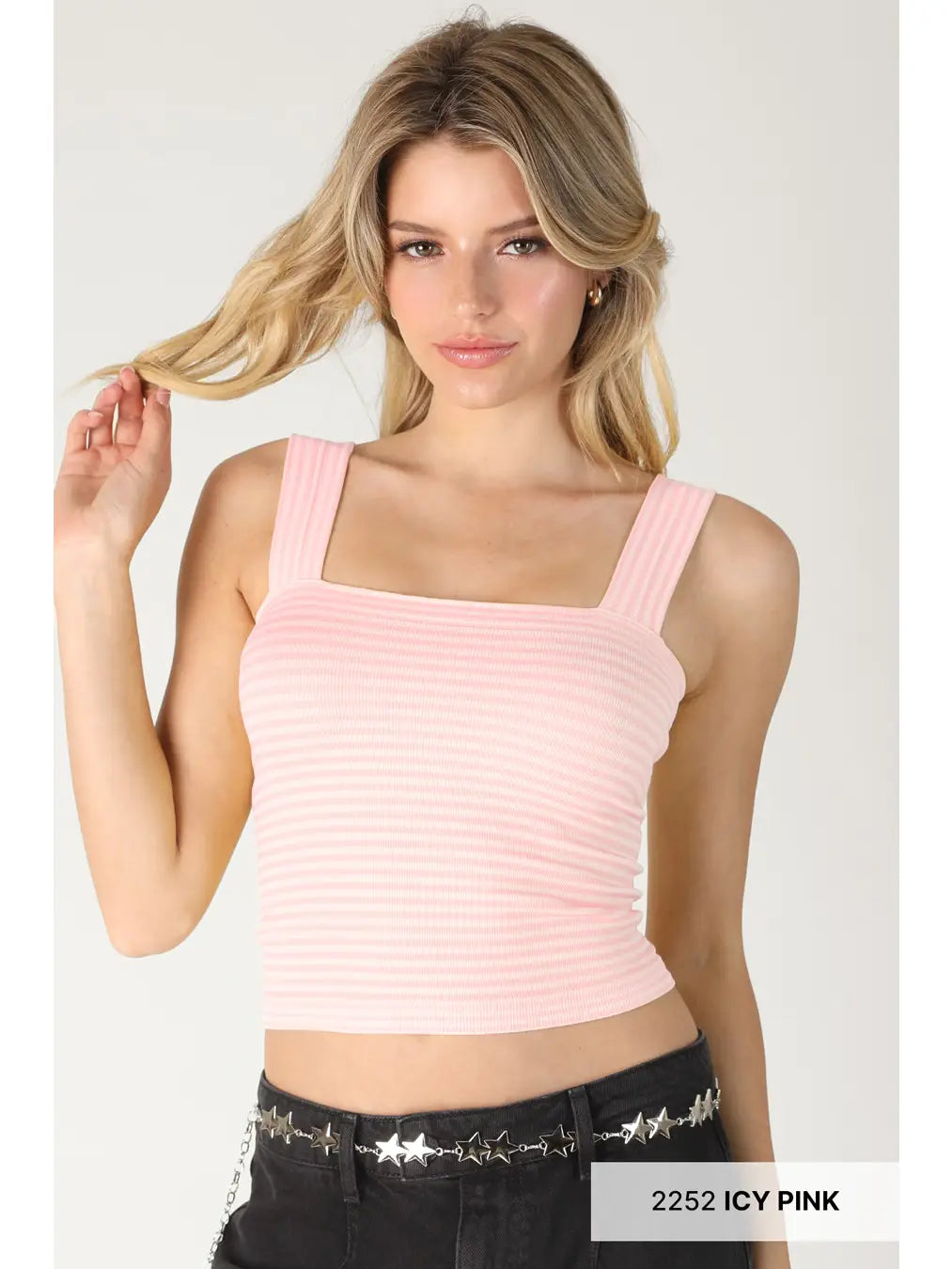 A blonde model wearing a light pink ribbed crop top with a square neckline and wide straps, paired with black jeans featuring a silver star belt. A text label in the bottom right corner reads '2252 ICY PINK'.