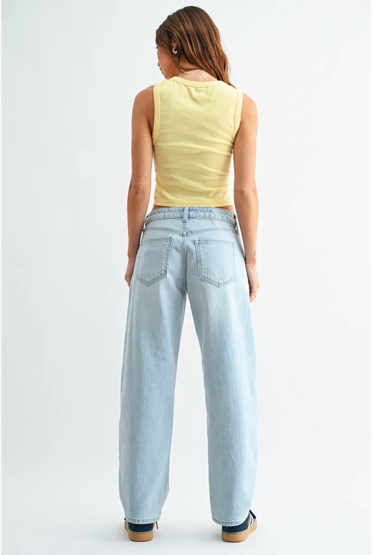 Woman wearing light blue jeans and a yellow sleeveless top on a white background
