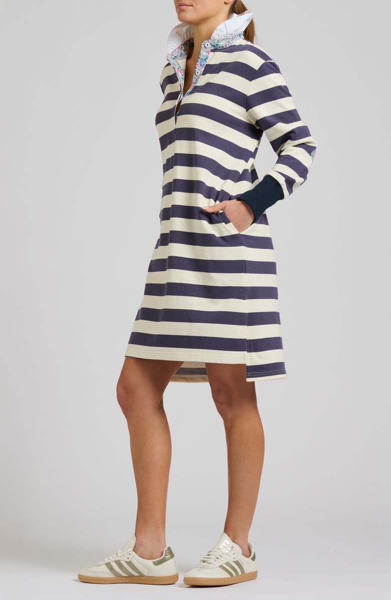 Person wearing a navy and white striped dress with a high collar on a plain background