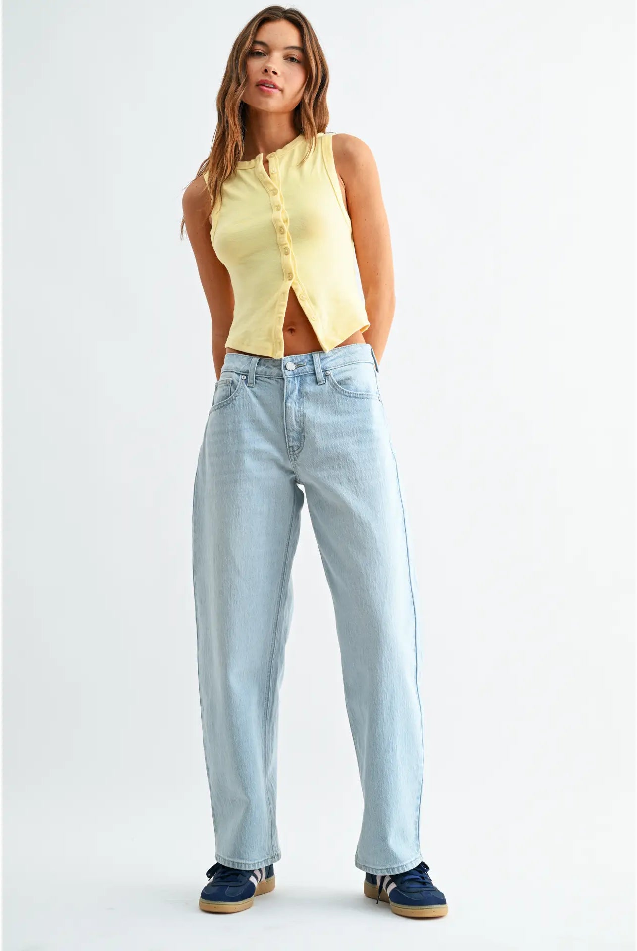 Woman wearing a yellow sleeveless top and light blue jeans on a white background
