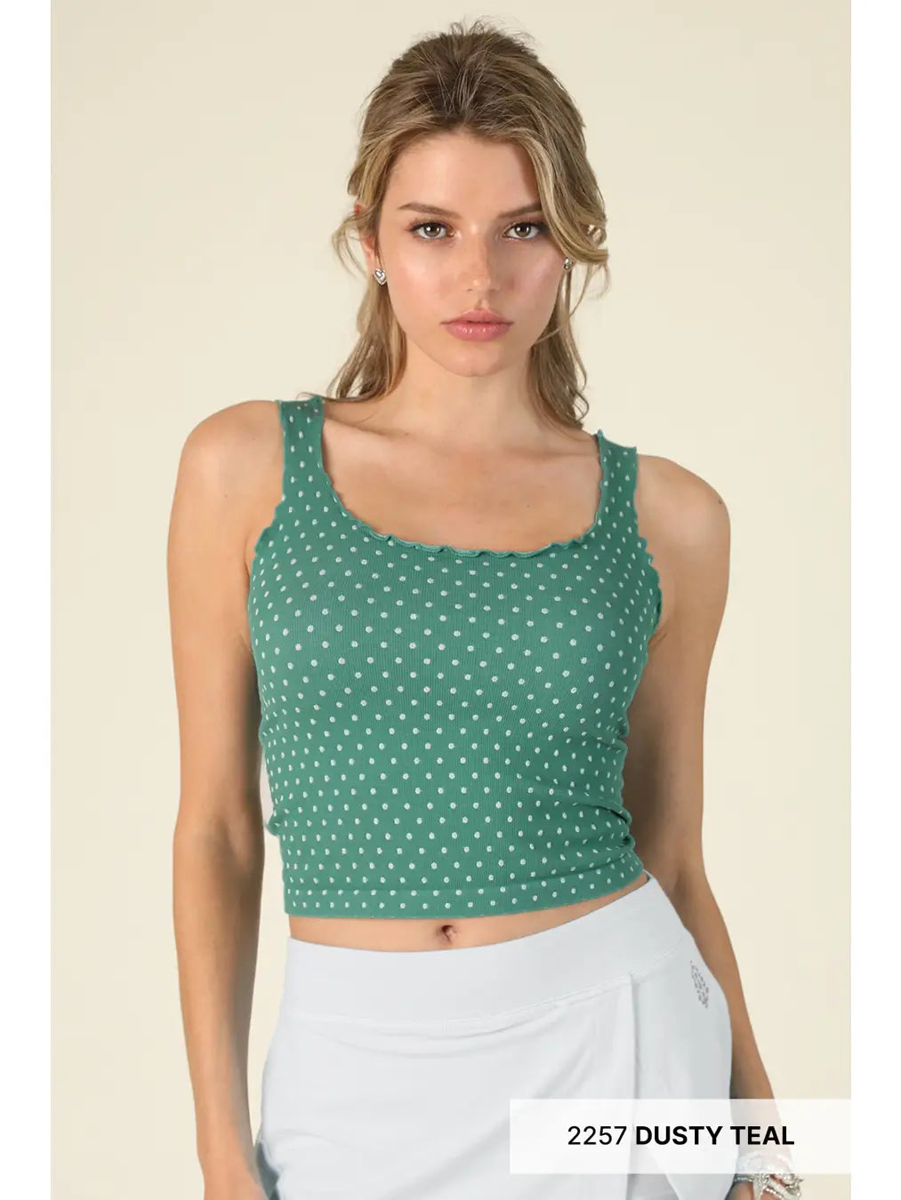 Woman wearing a green polka dot crop top against a beige background