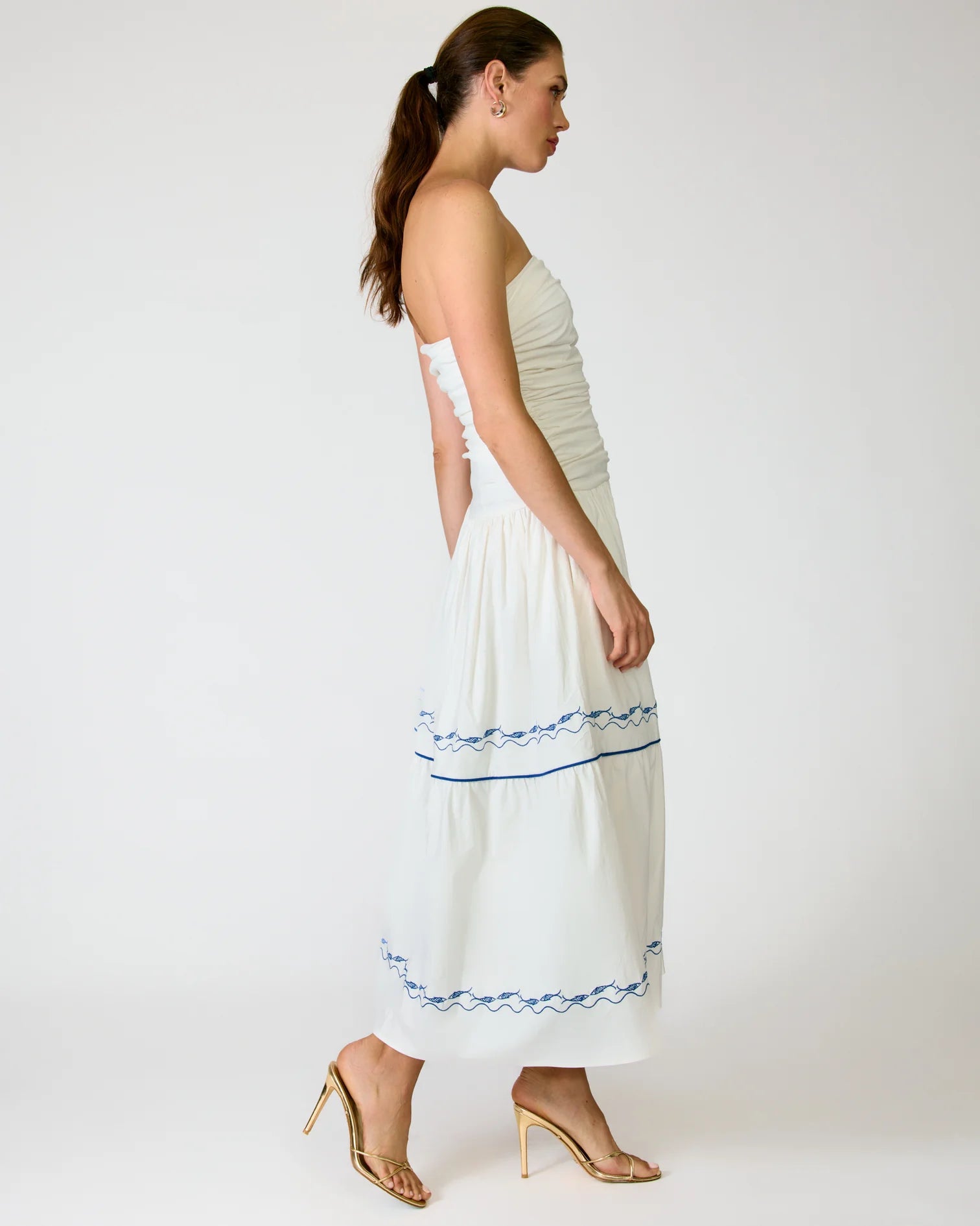 Woman wearing a white strapless dress with blue embroidery on a white background