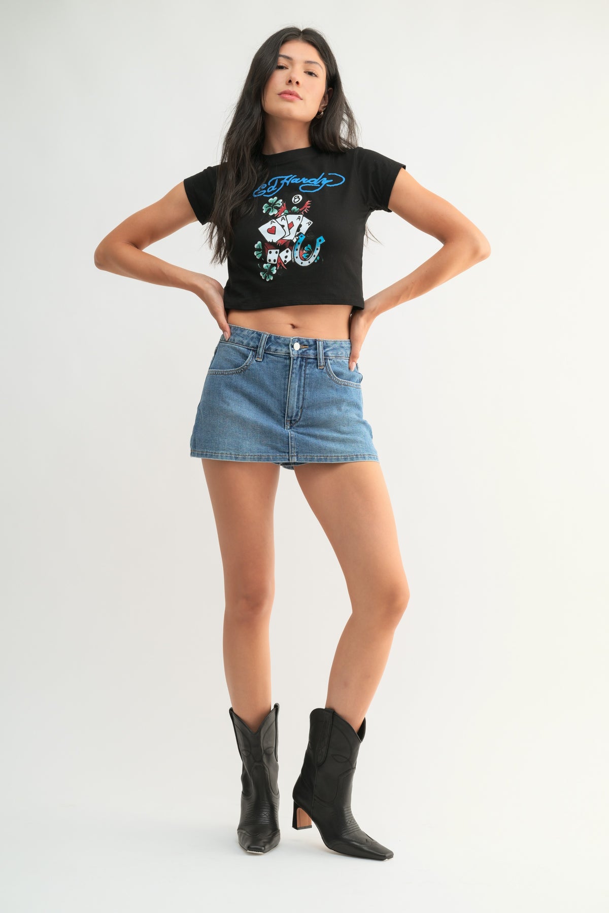 Woman wearing a black t-shirt with graphic design, blue denim skirt, and black boots on a white background