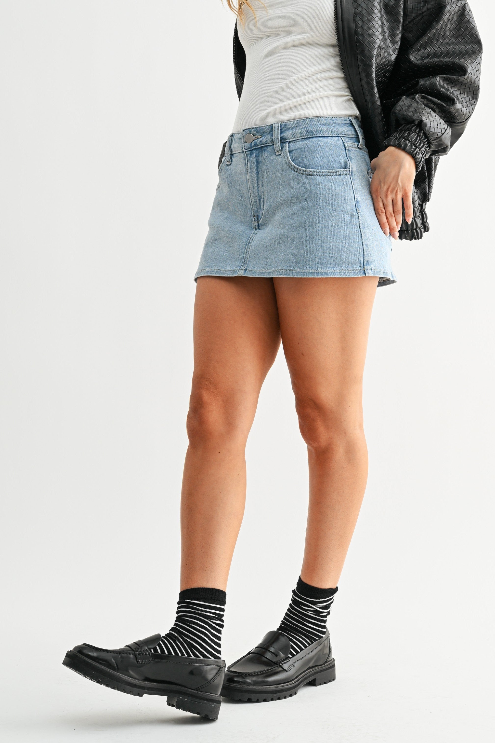 Woman wearing a black jacket, white shirt, denim skirt, and black boots on a white background