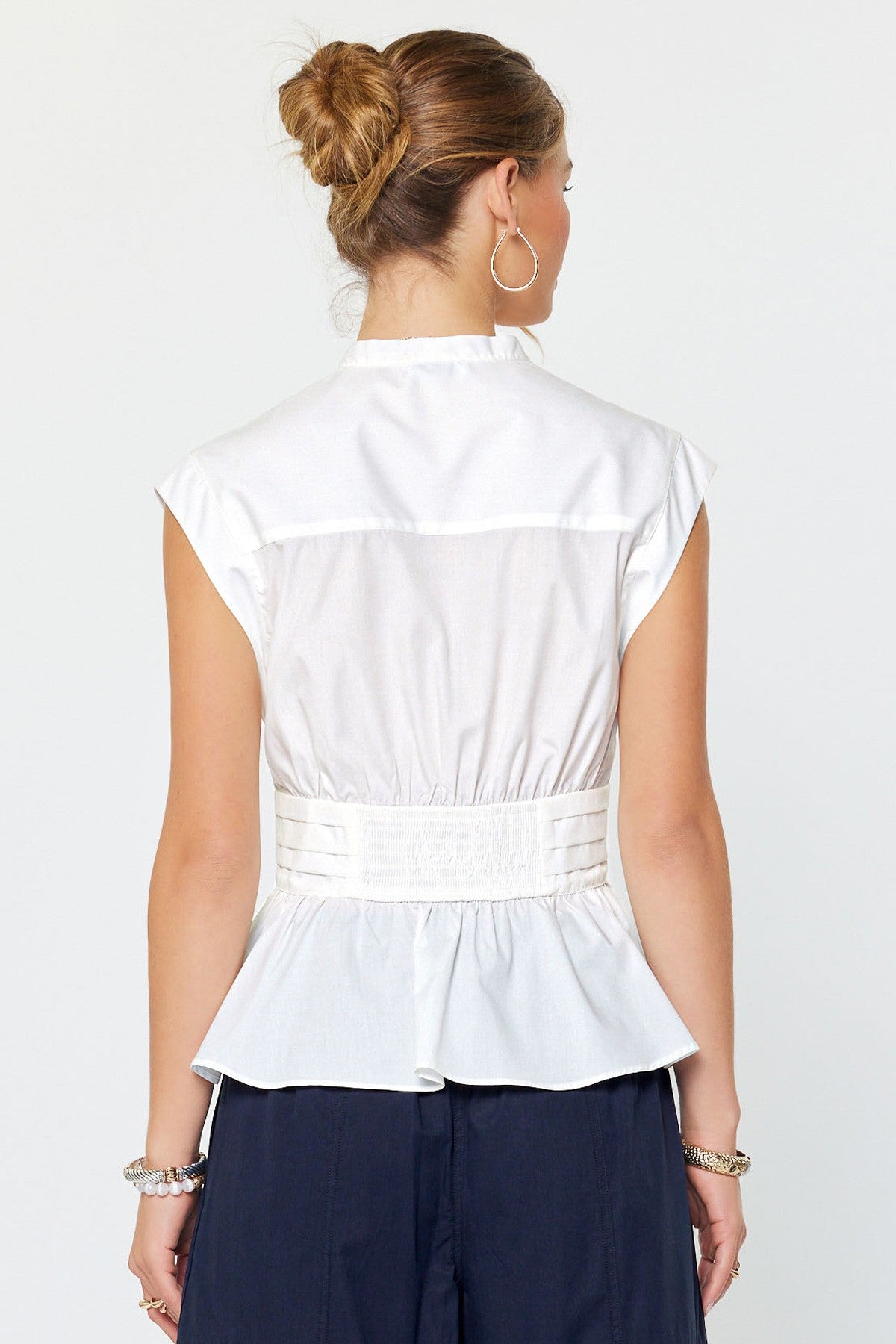 Woman wearing a white sleeveless top with a belt and navy pants on a white background