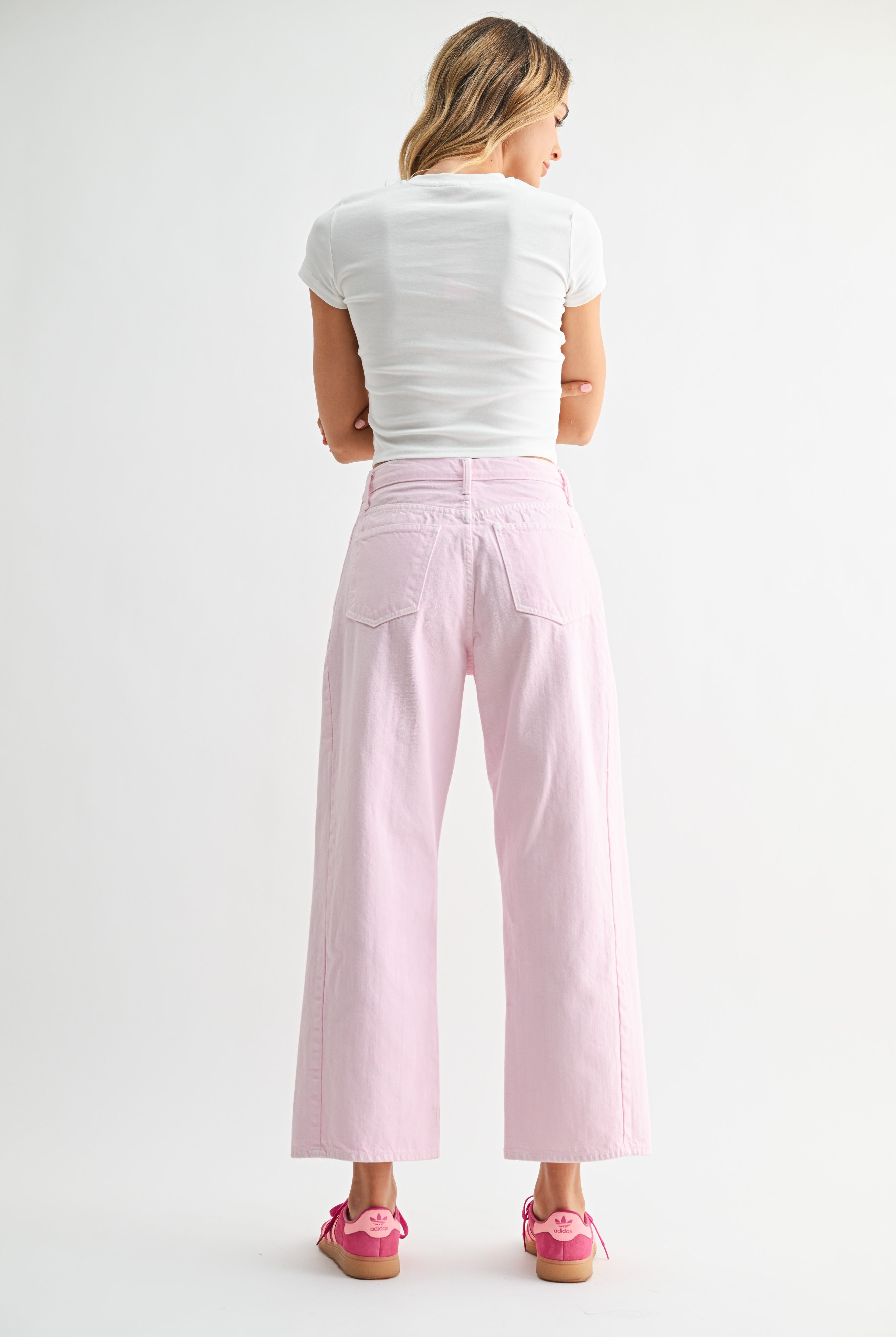 Woman wearing light pink pants and a white top on a plain background
