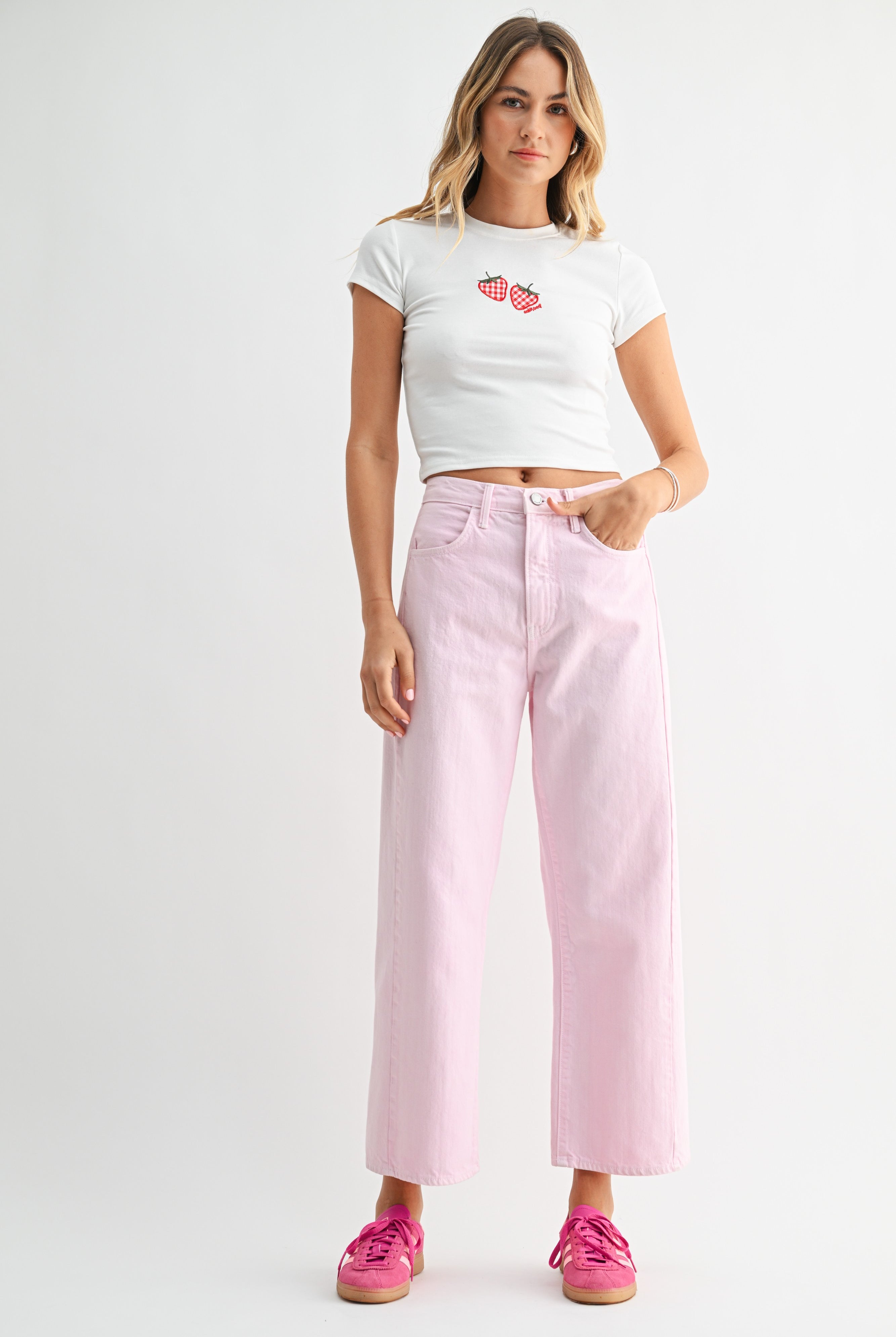 Woman wearing a white crop top with red graphics and pink high-waisted jeans on a white background