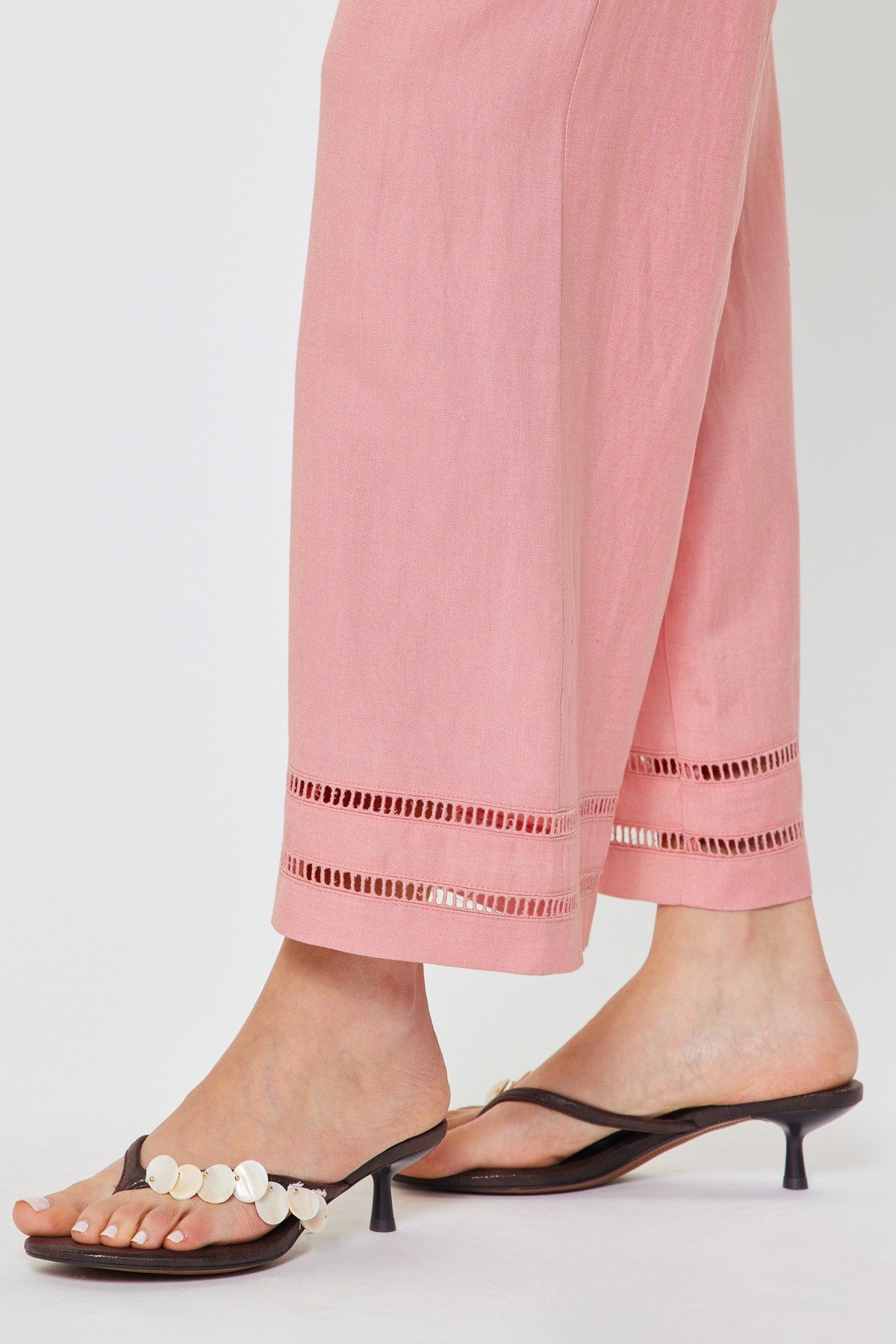 Person wearing pink pants with lace details and black high-heeled sandals on a white background