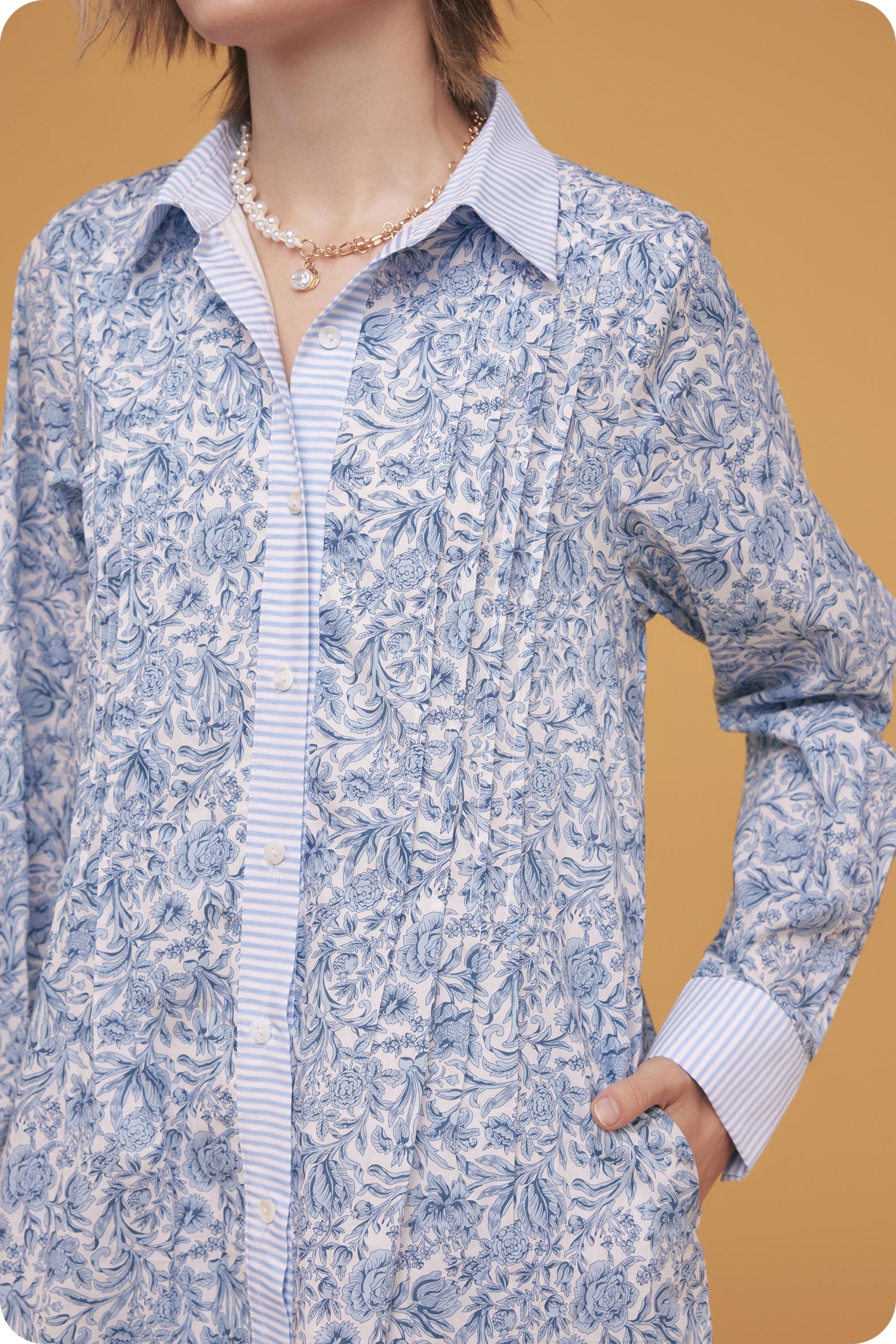 Person wearing a blue floral dress over a striped shirt against a mustard yellow background