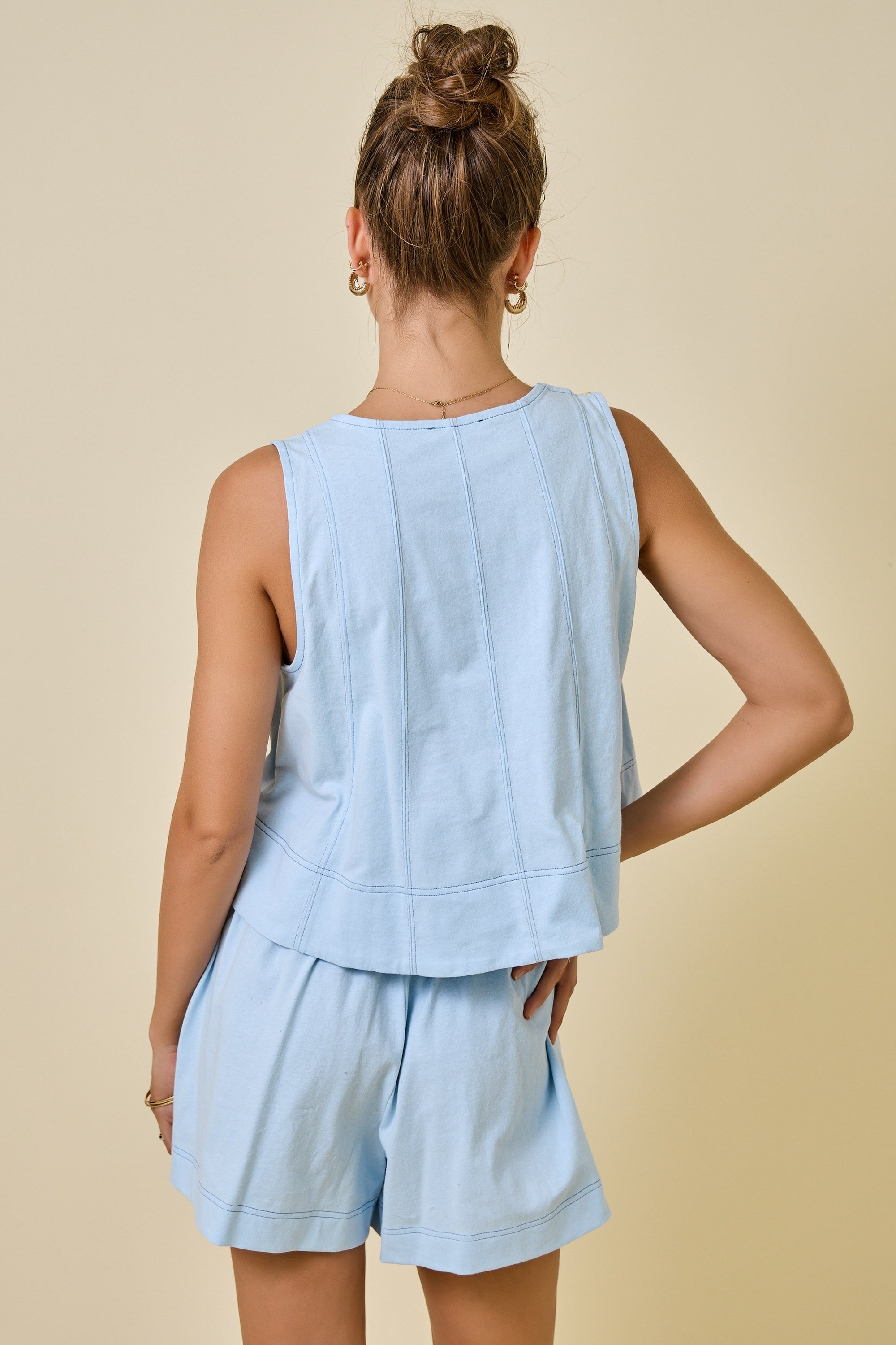 Woman wearing a light blue sleeveless top and shorts set on a beige background