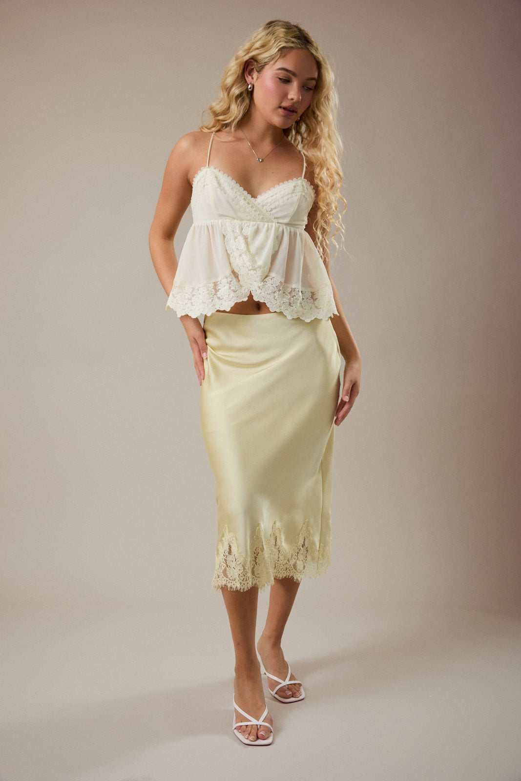 Woman wearing a white lace top and light yellow skirt against a plain background