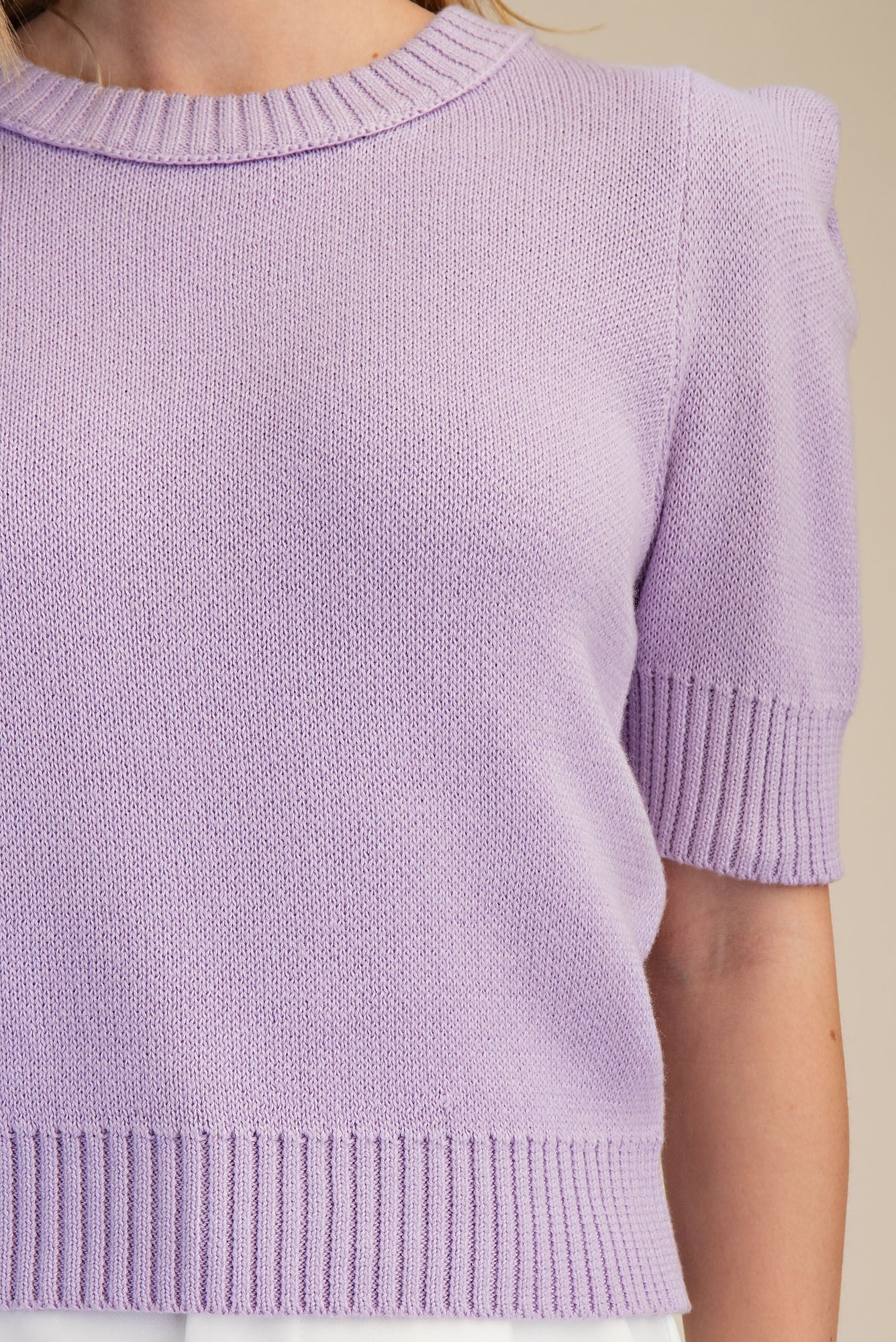 Close-up of a person wearing a light purple knitted sweater with a plain background