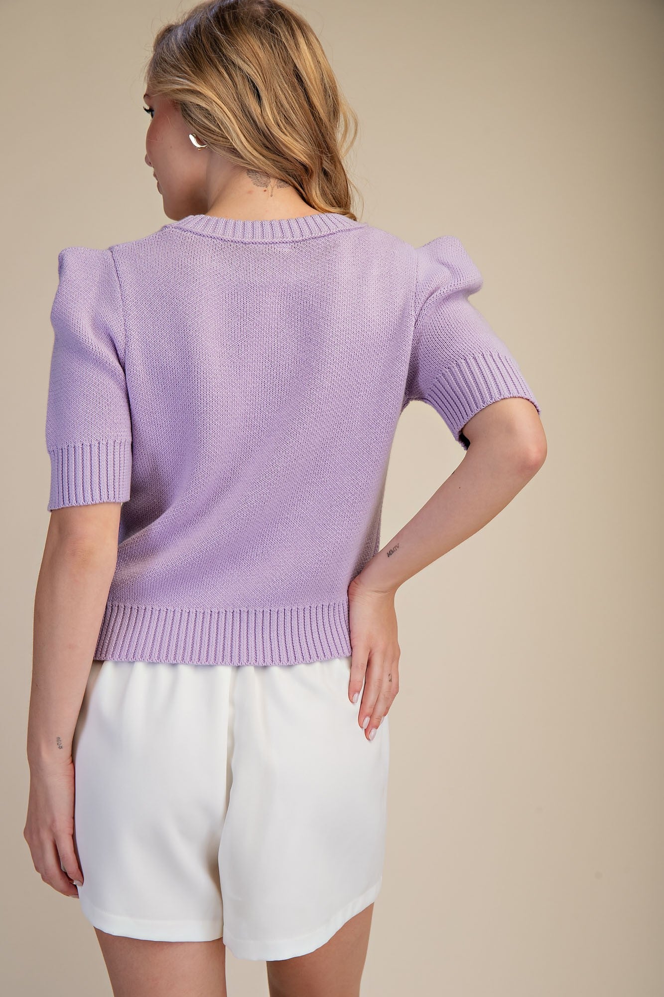 Person wearing a light purple sweater and white shorts on a beige background