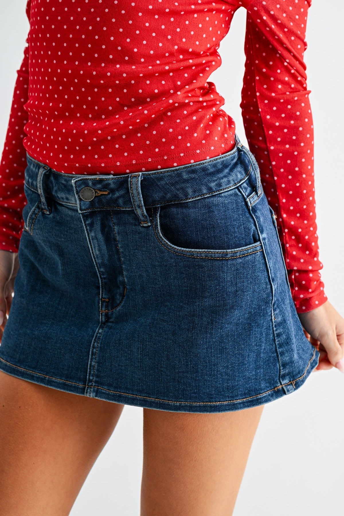 Person wearing a red polka dot shirt and blue denim skirt on a white background