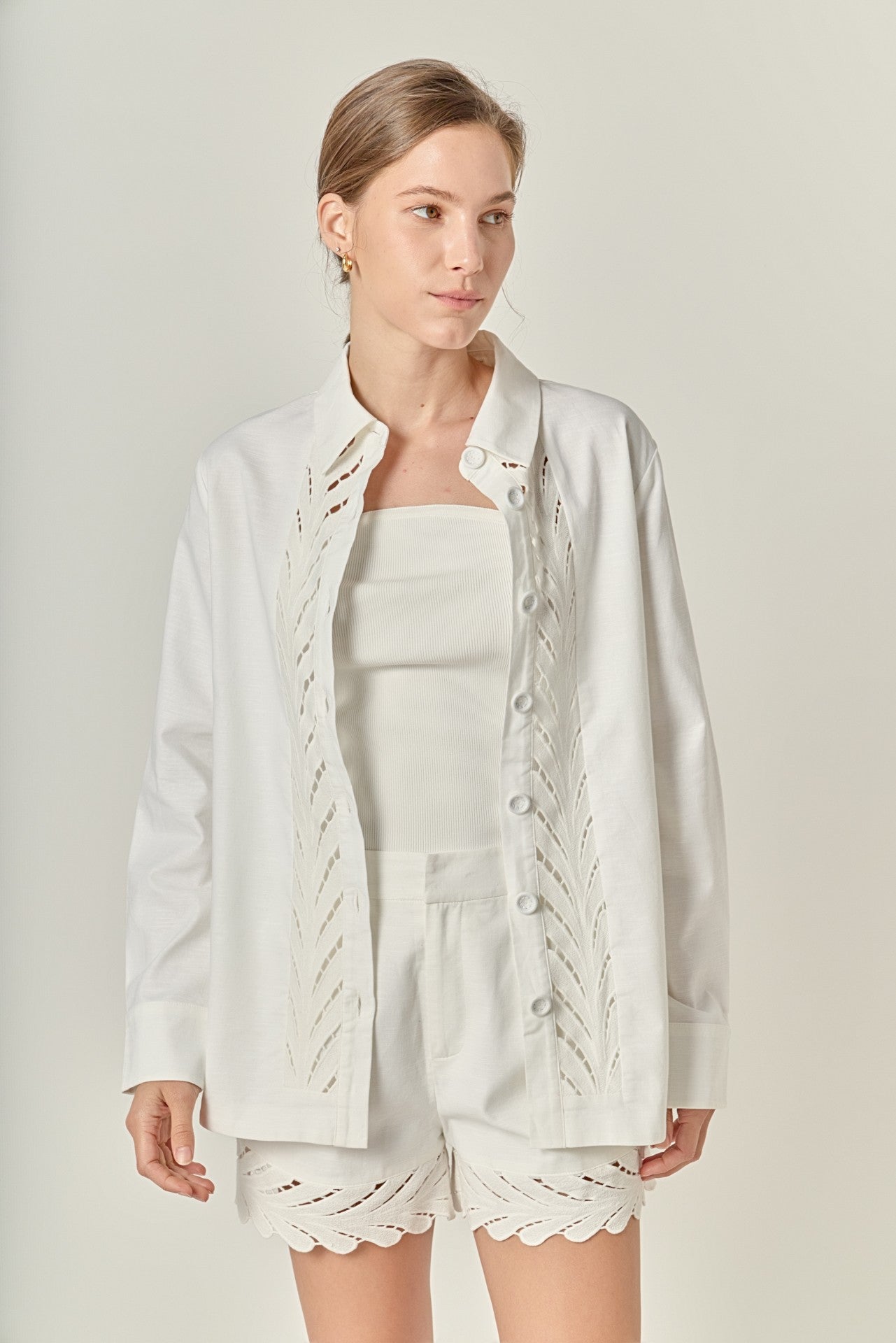 Woman wearing a white outfit with lace details on a plain background