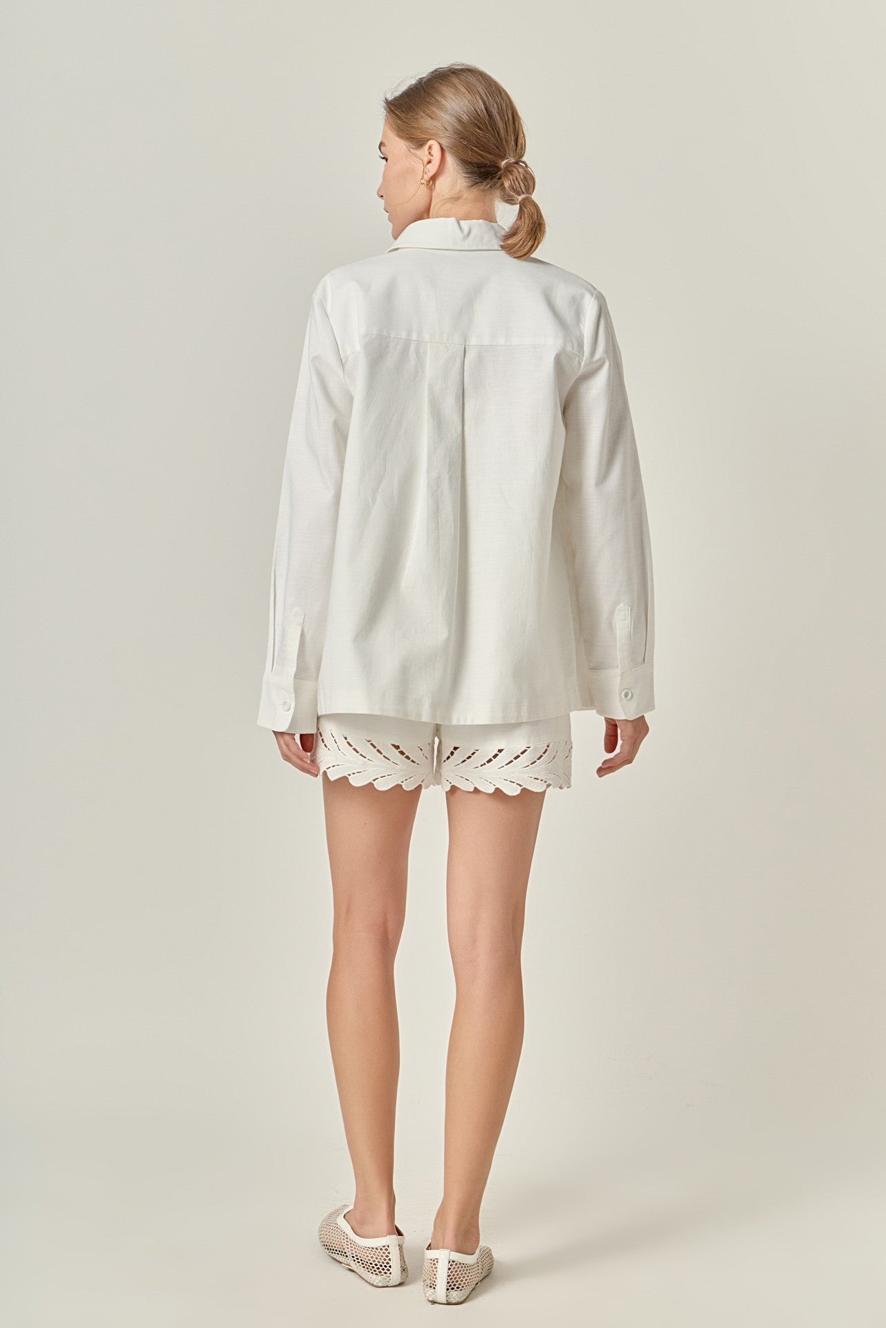 Woman wearing a light-colored shirt and shorts on a plain background