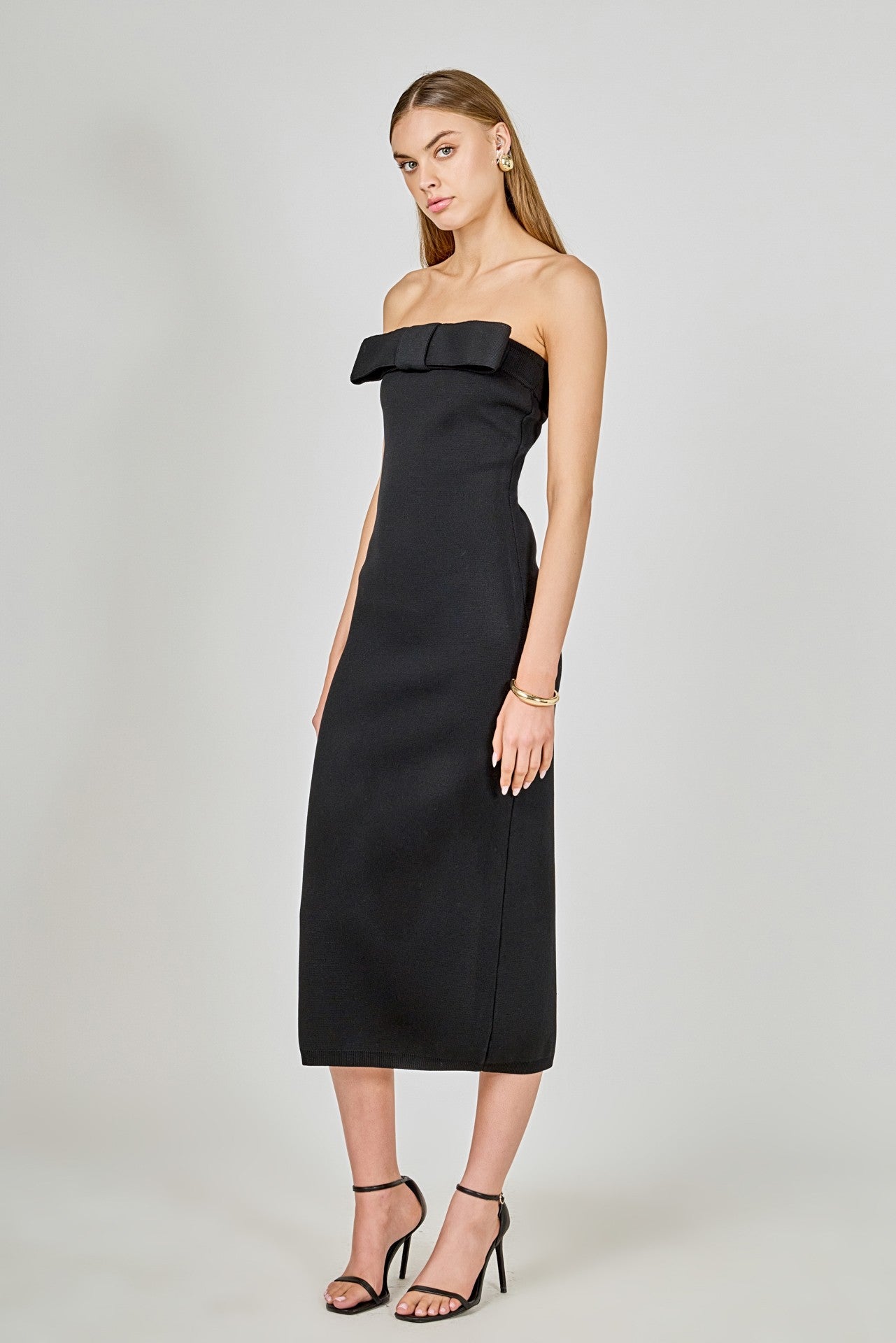 Woman wearing a black strapless dress with a bow detail on a white background