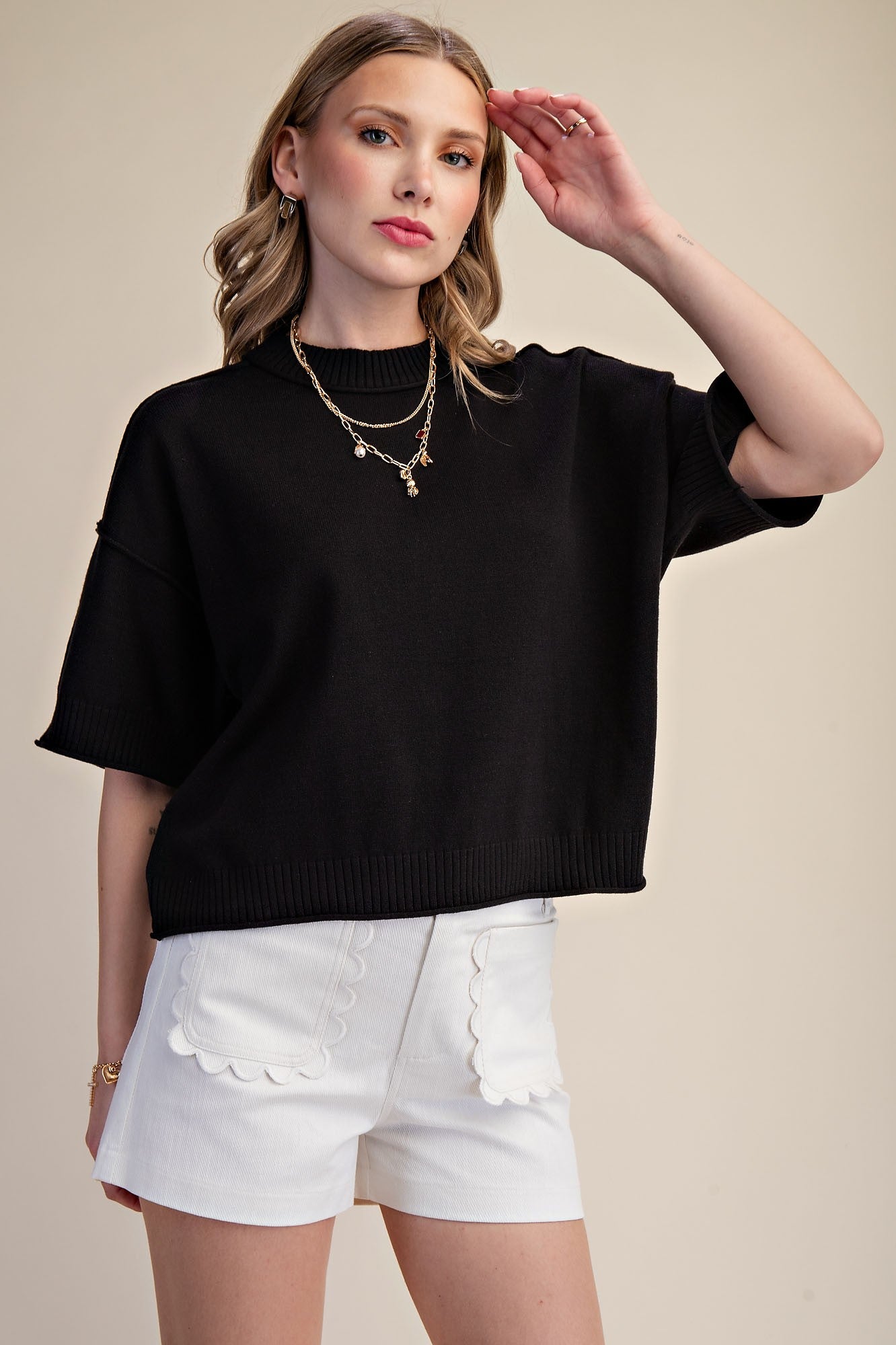 Woman wearing a black sweater and white shorts on a beige background