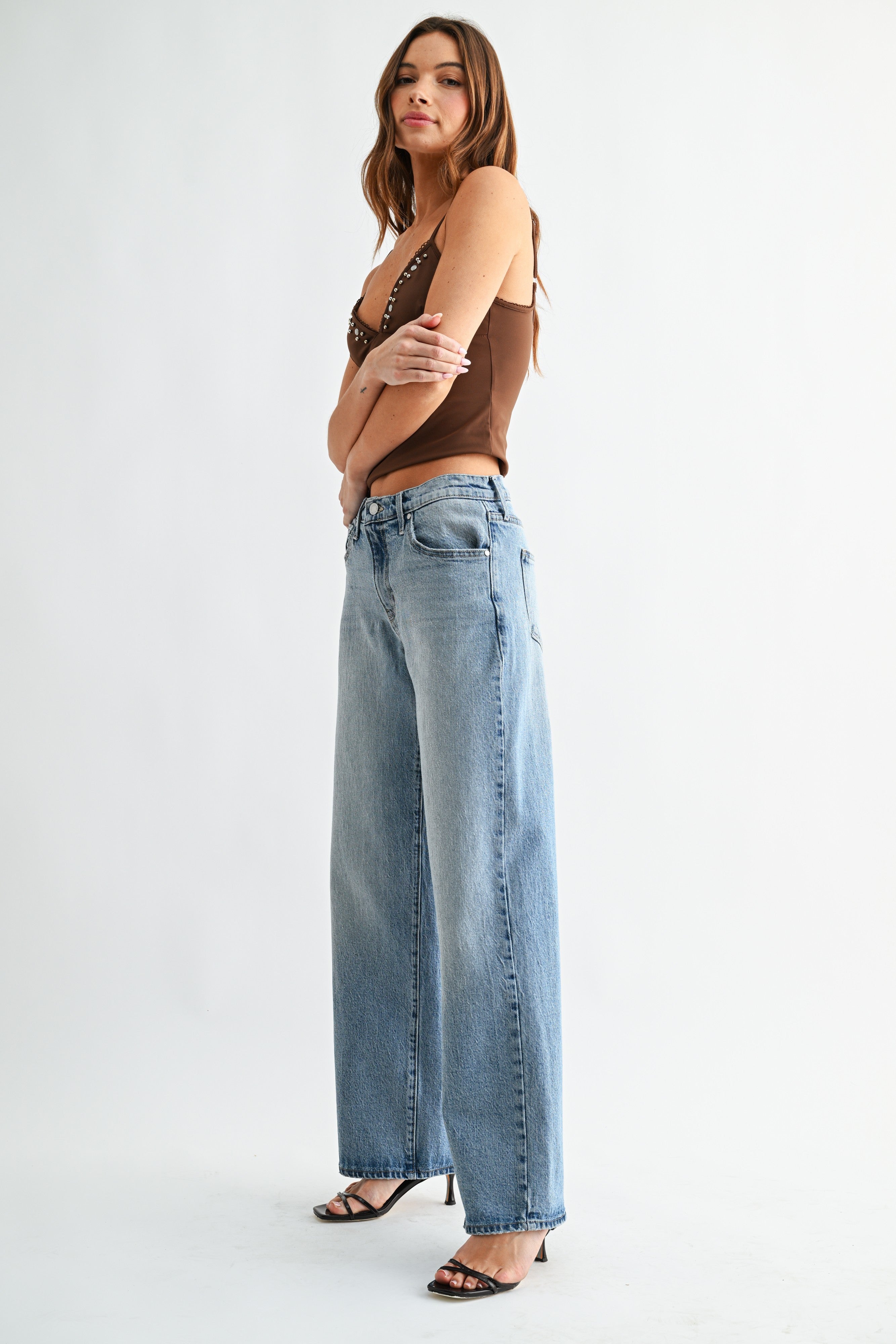 Woman wearing a brown top and light blue jeans on a white background