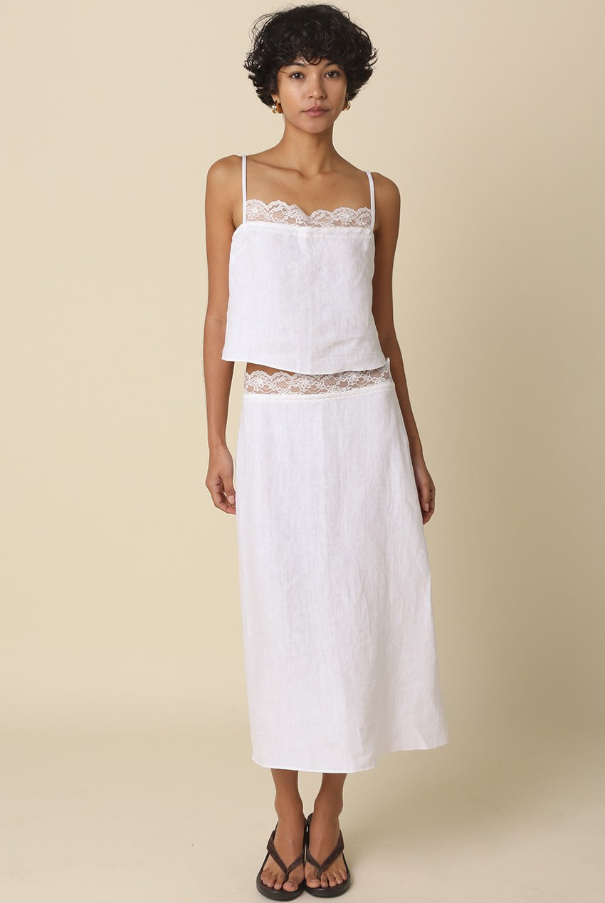 Woman wearing a white top and skirt with lace details on a beige background