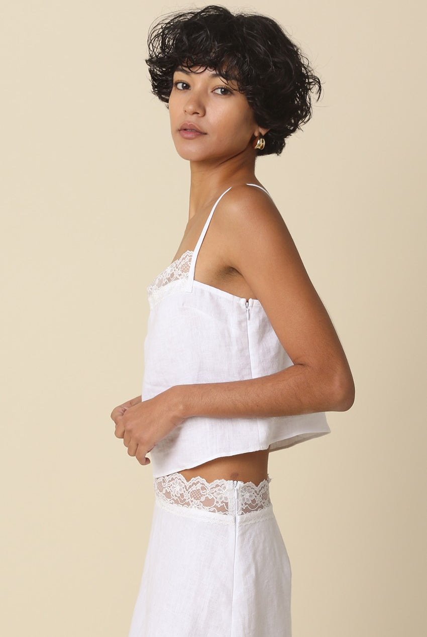 Woman wearing a white lace-trimmed top and pants against a beige background
