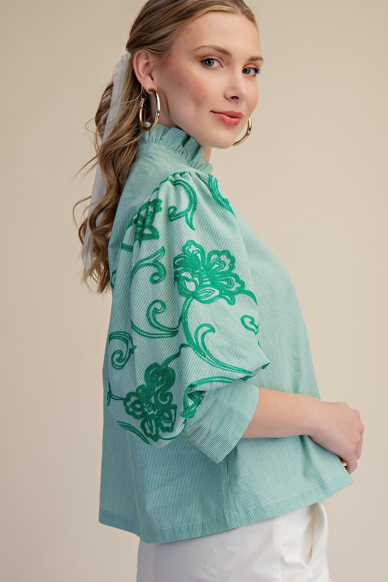 Woman wearing a light blue blouse with green floral patterns on a beige background