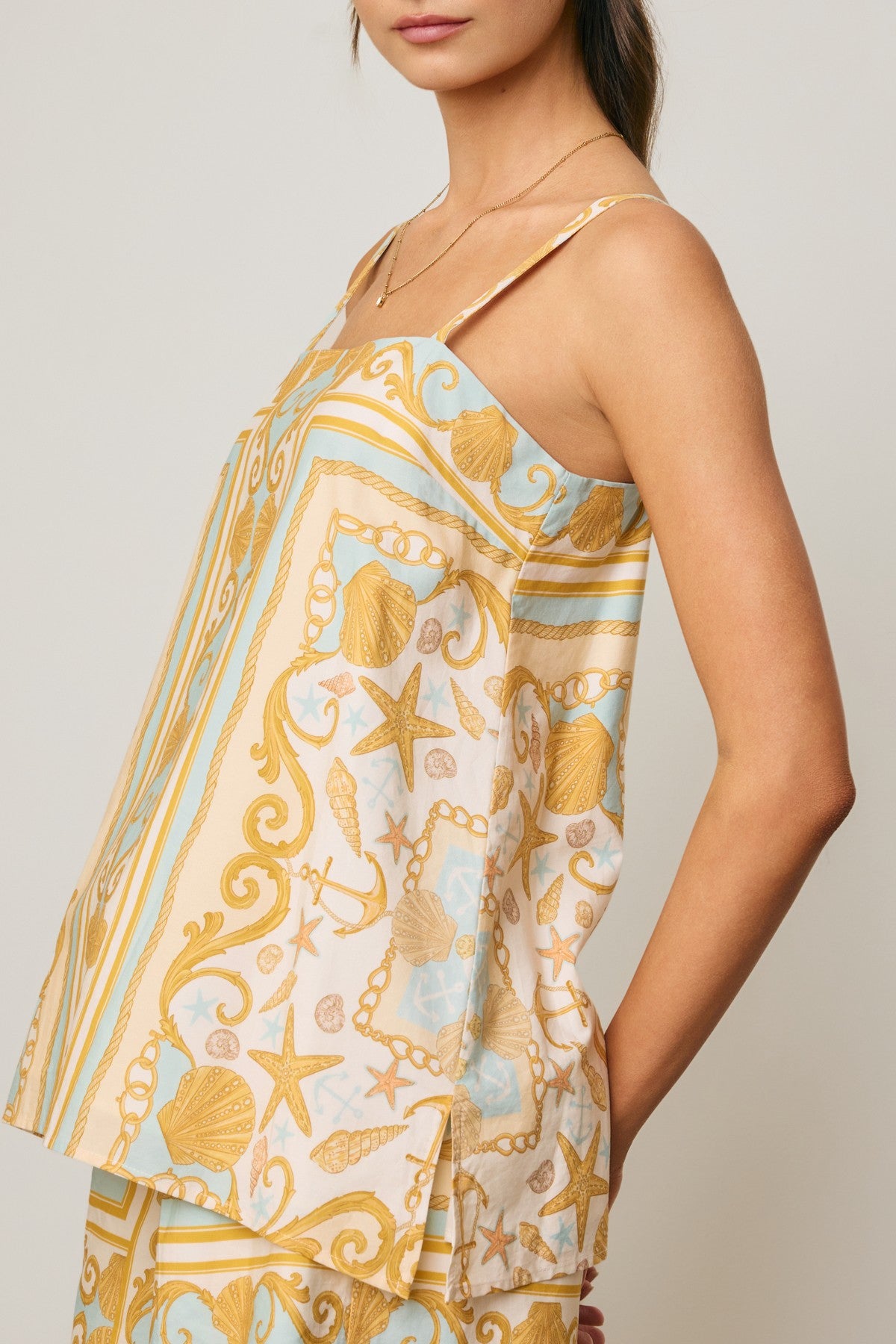 Woman wearing a sleeveless top with a shell pattern on a plain background