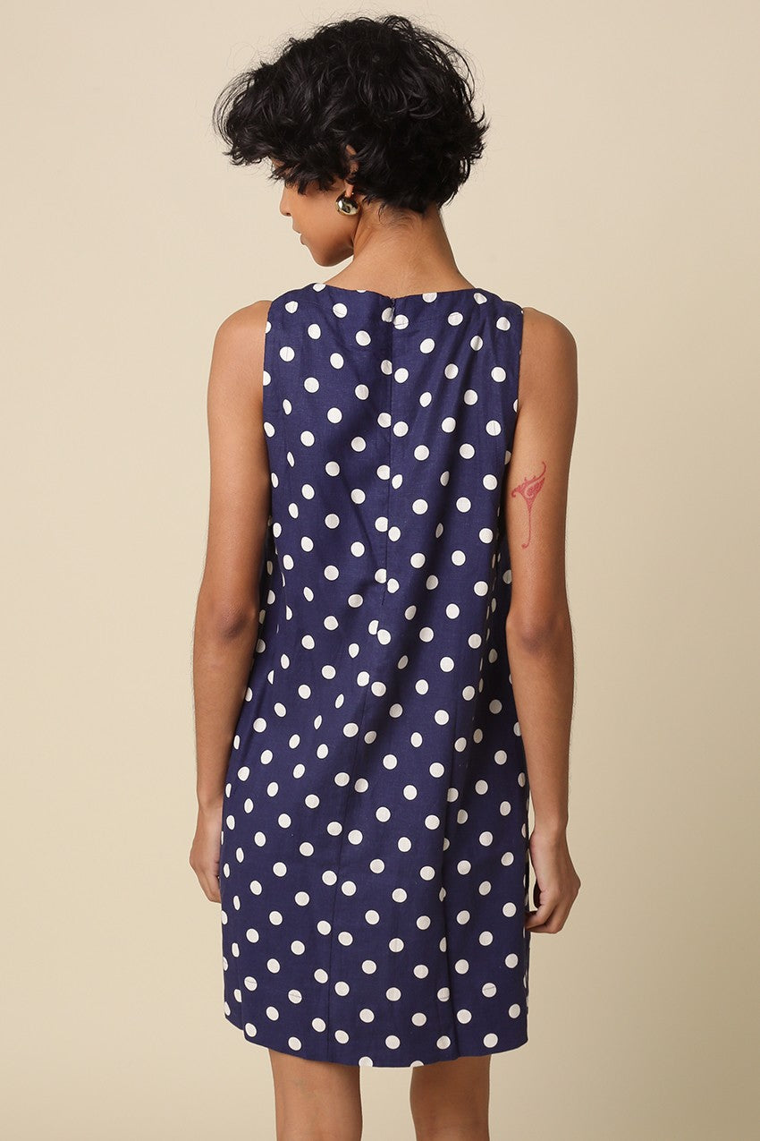 Woman wearing a navy dress with white polka dots against a beige background