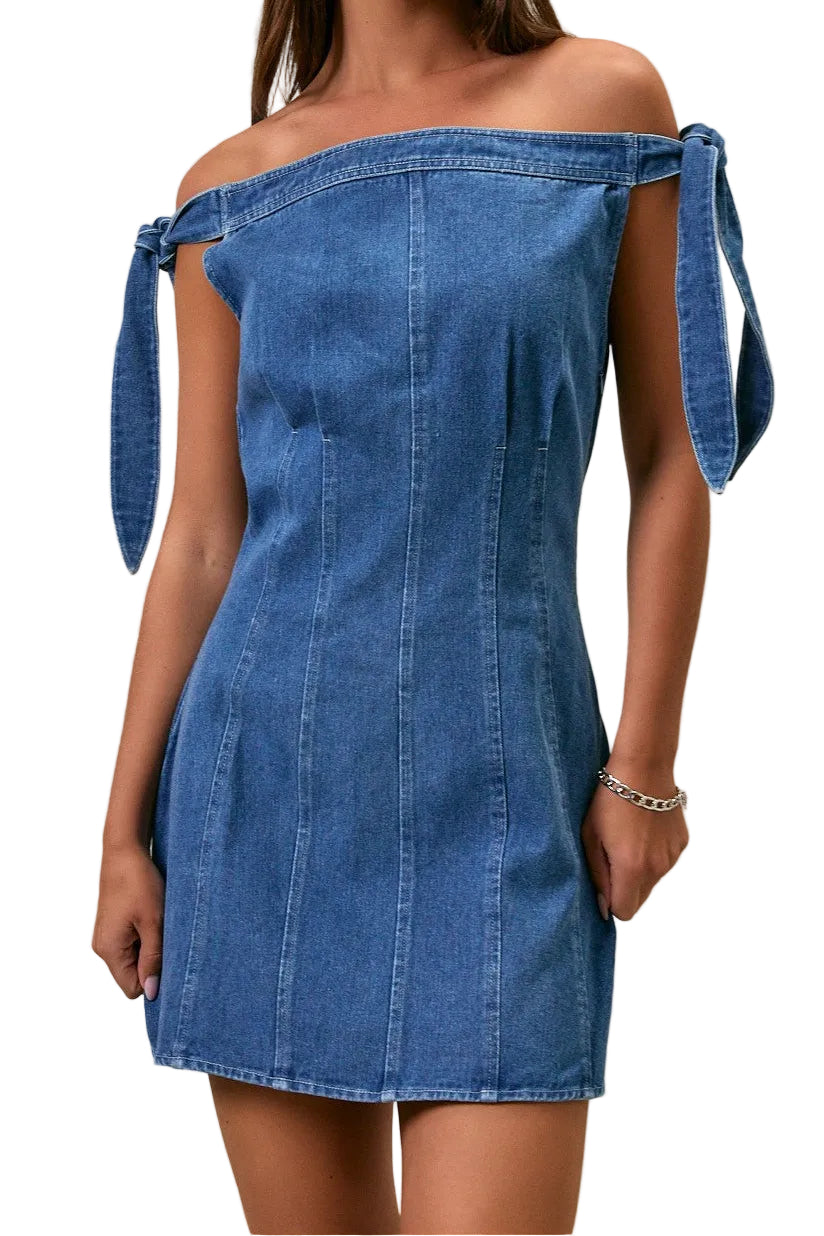 Woman wearing a blue denim dress with shoulder ties against a neutral background