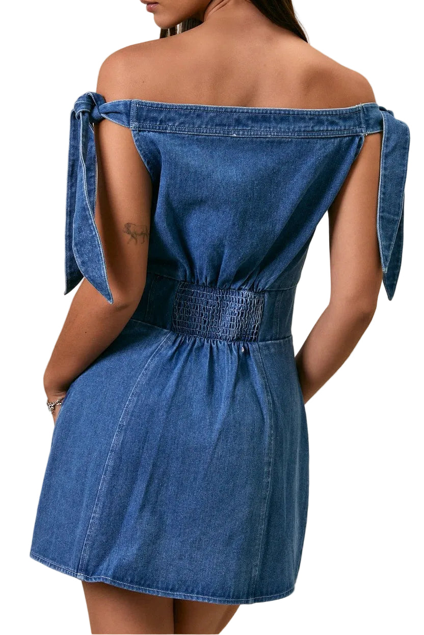 Woman wearing a blue denim dress with bow straps on a beige background