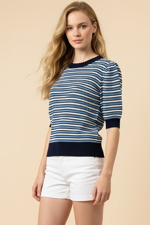 Woman wearing a blue and white striped sweater with white shorts on a beige background
