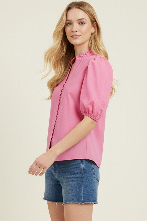 Woman wearing a pink blouse with puff sleeves and denim shorts on a beige background