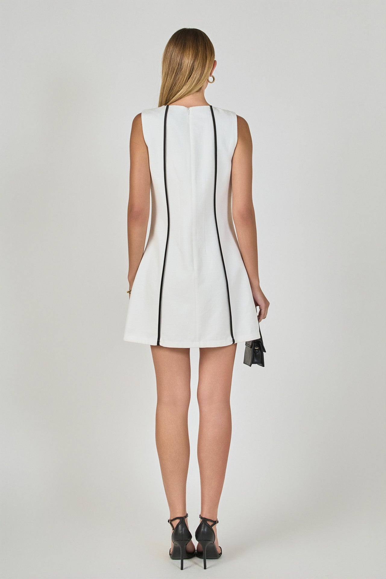 Woman wearing a white sleeveless dress with black trim on a plain background
