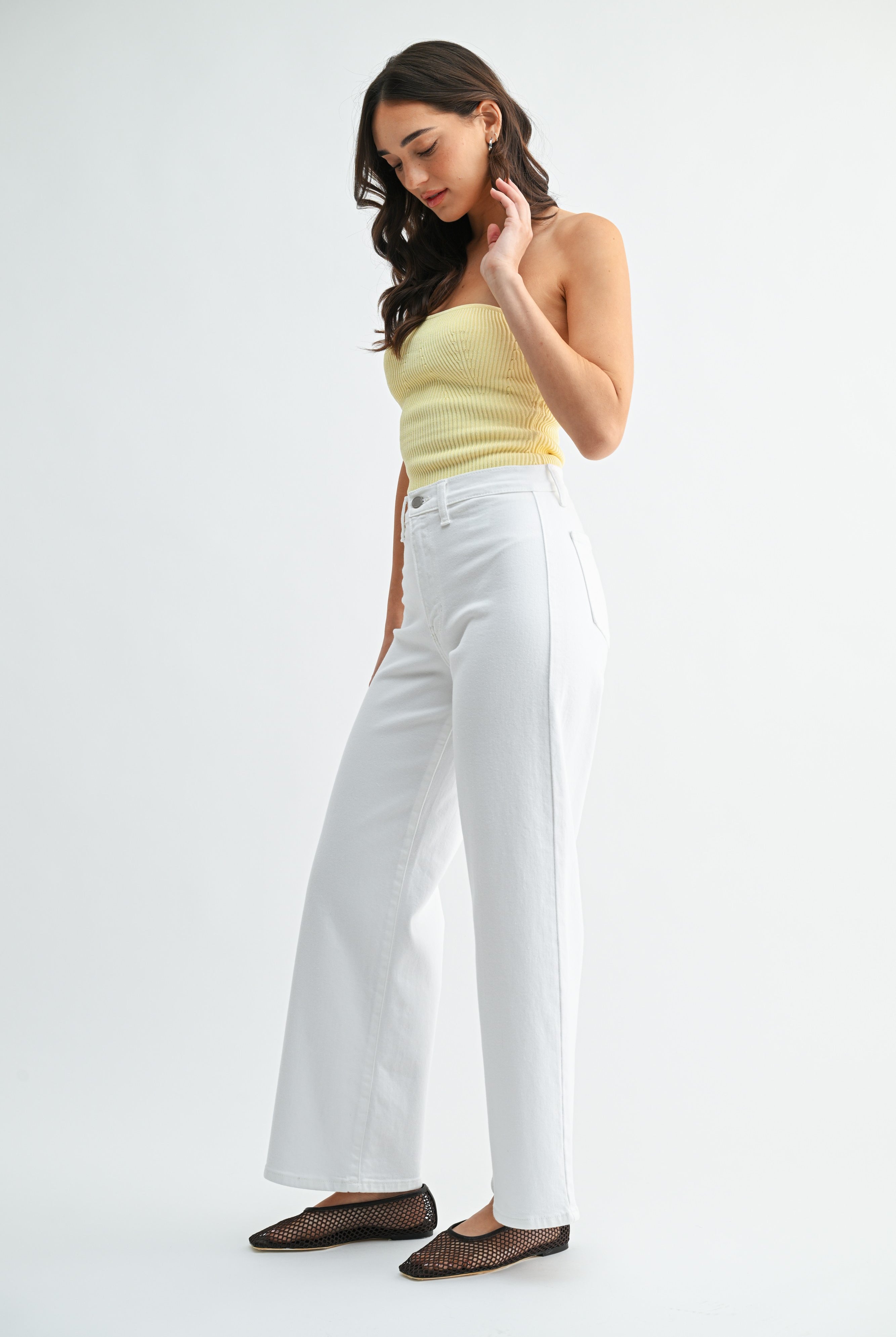 Woman wearing a yellow top and white pants on a white background