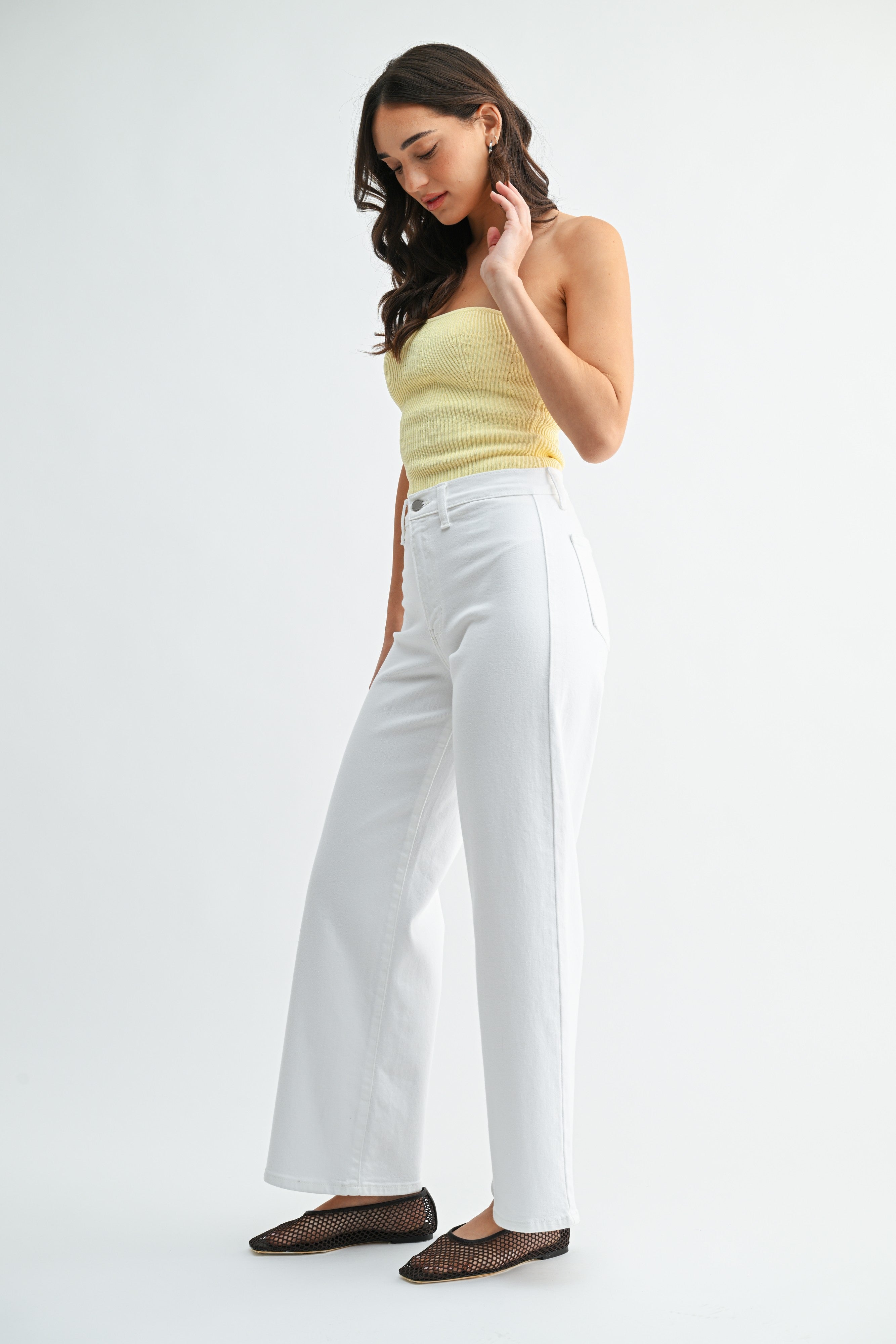 Woman wearing a yellow top and white pants on a white background