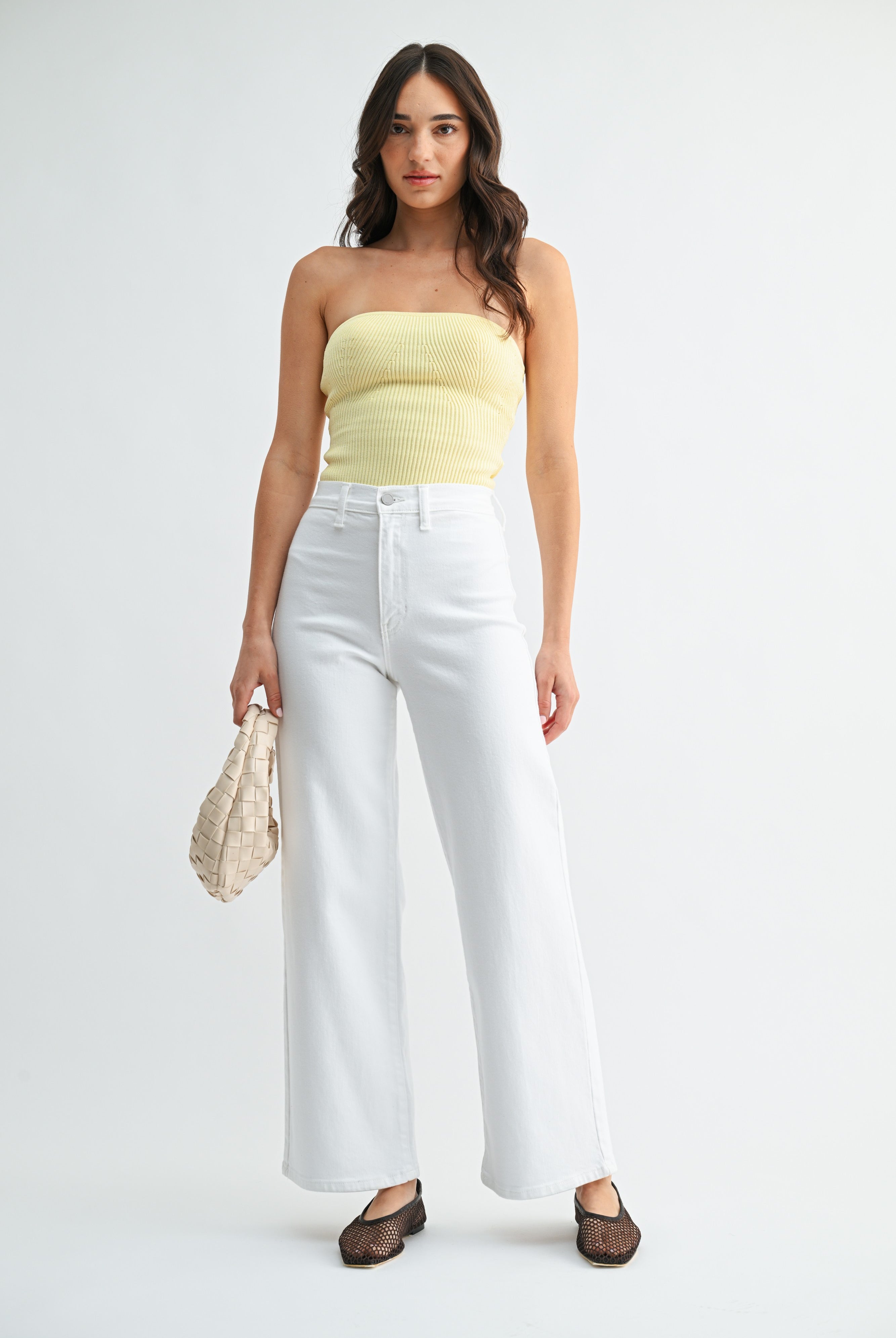 Woman wearing a strapless yellow top and white pants on a white background
