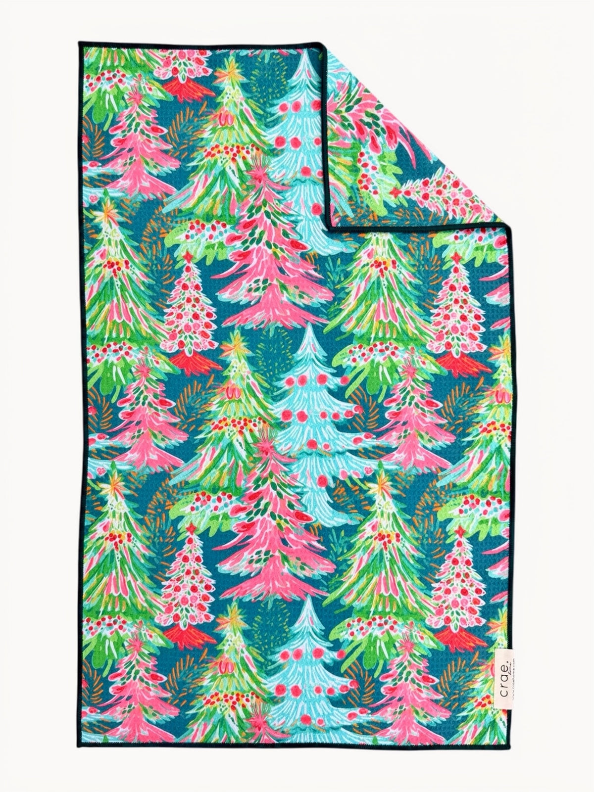 A folded blanket featuring a colorful Christmas tree pattern on a dark teal background, with a small white tag on the lower edge.