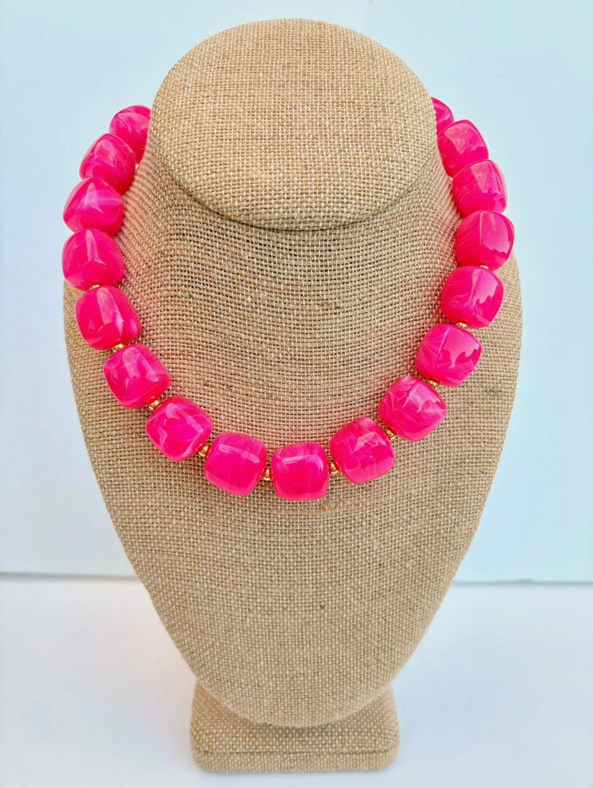 Necklace with bright pink beads on a beige mannequin bust against a light blue background