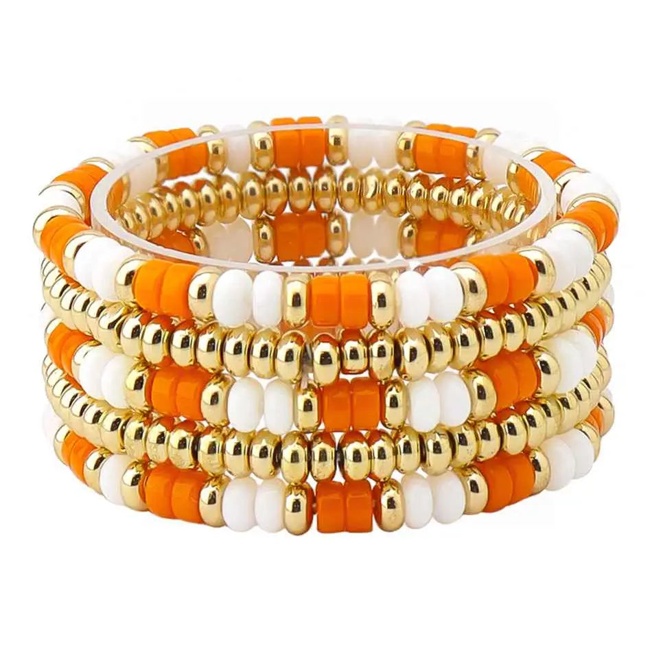 A stack of 4 beaded stretch bracelets featuring alternating orange and white beads with shiny gold metallic spacer beads, set against a plain white background.