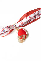 Decorative twilly scarf with a red and gold helmet pendant on a white background
