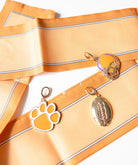 Two keychains, one shaped like a paw print and the other resembling a football, on a orange fabric background.