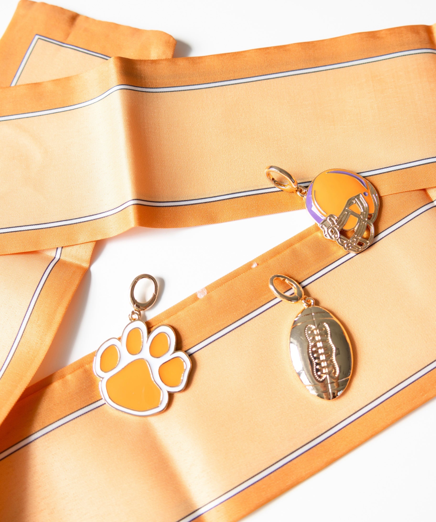 Two keychains, one shaped like a paw print and the other resembling a football, on a orange fabric background.