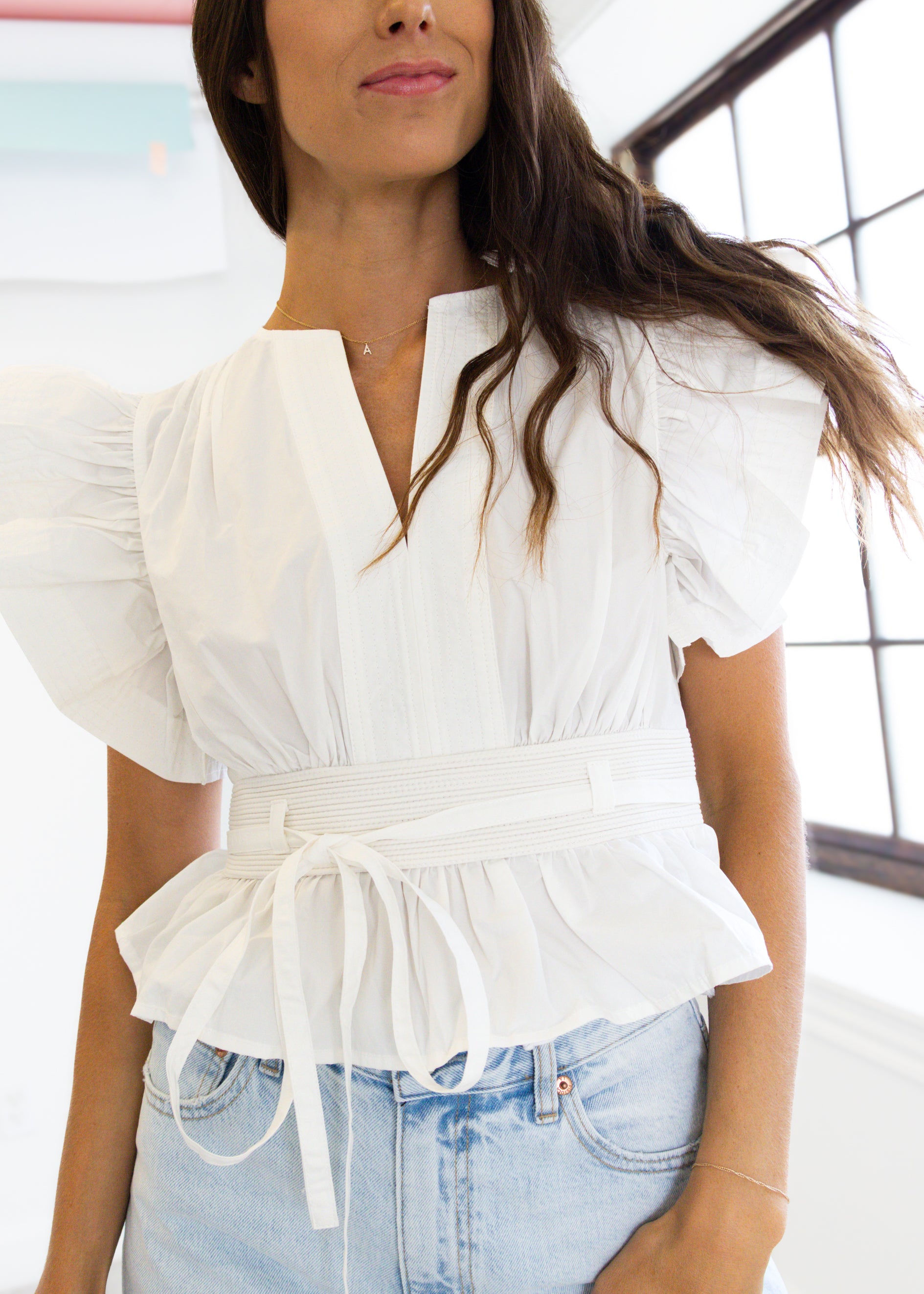Woman wearing a white blouse with puffed sleeves and light blue jeans indoors.