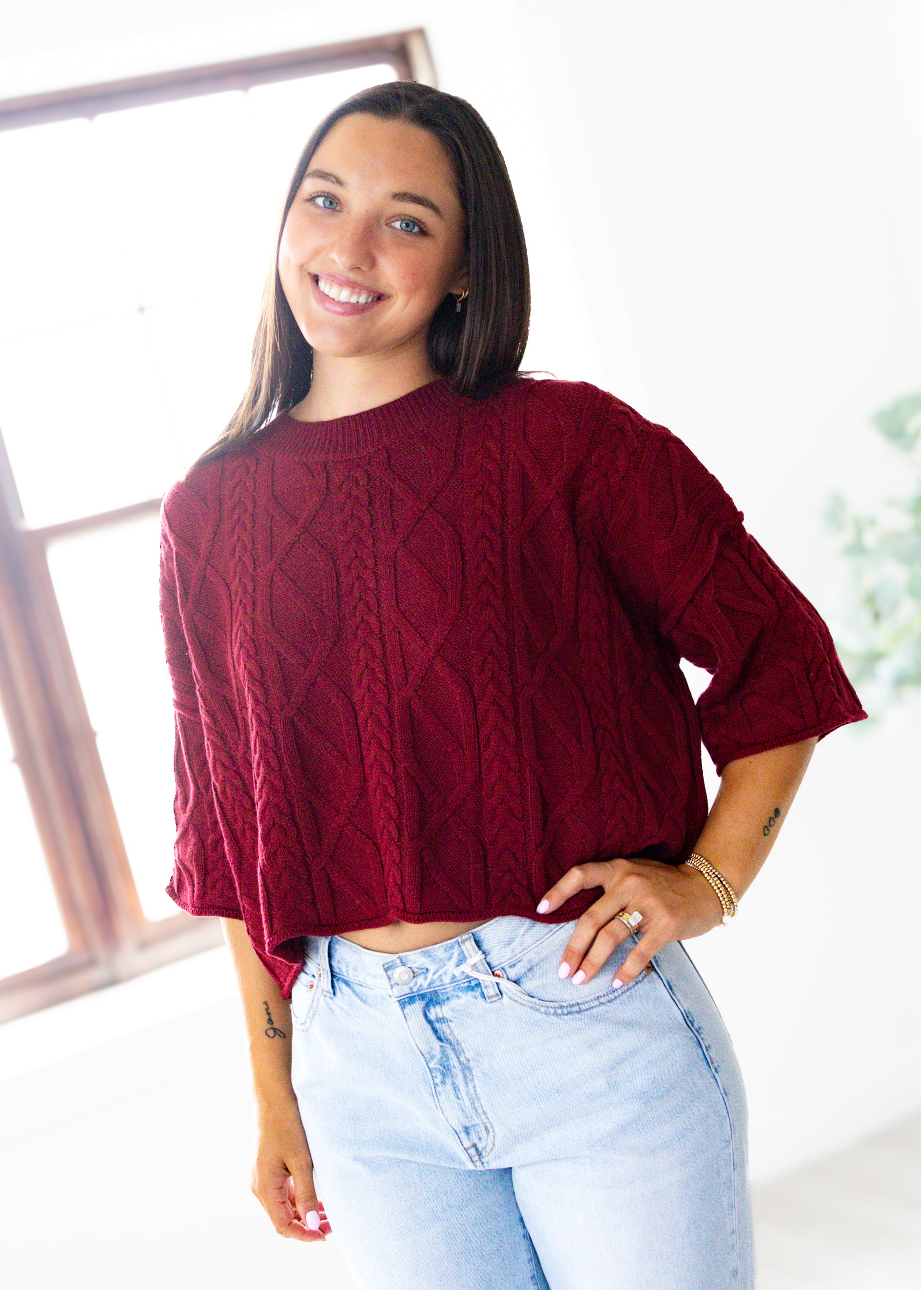 Woman wearing a burgundy sweater and light blue jeans indoors.