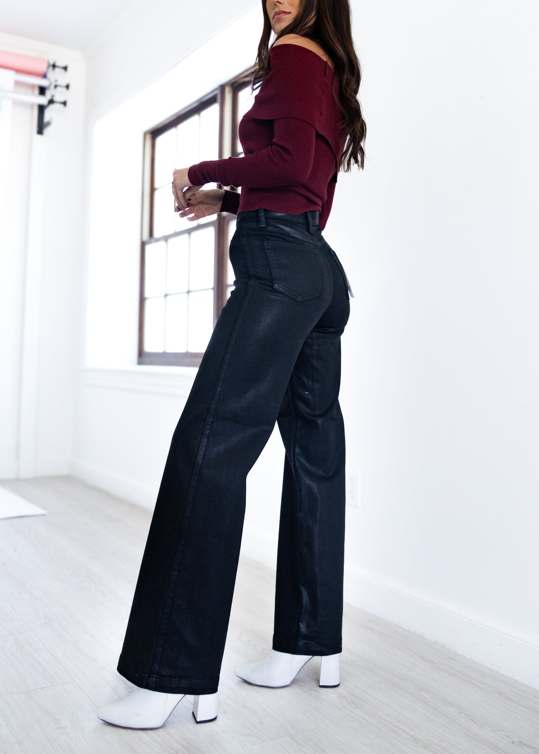 Person wearing a burgundy off-shoulder top and black wide-leg pants in a minimal indoor setting.