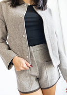 Person wearing a gray coat over a black top and shorts on a white background