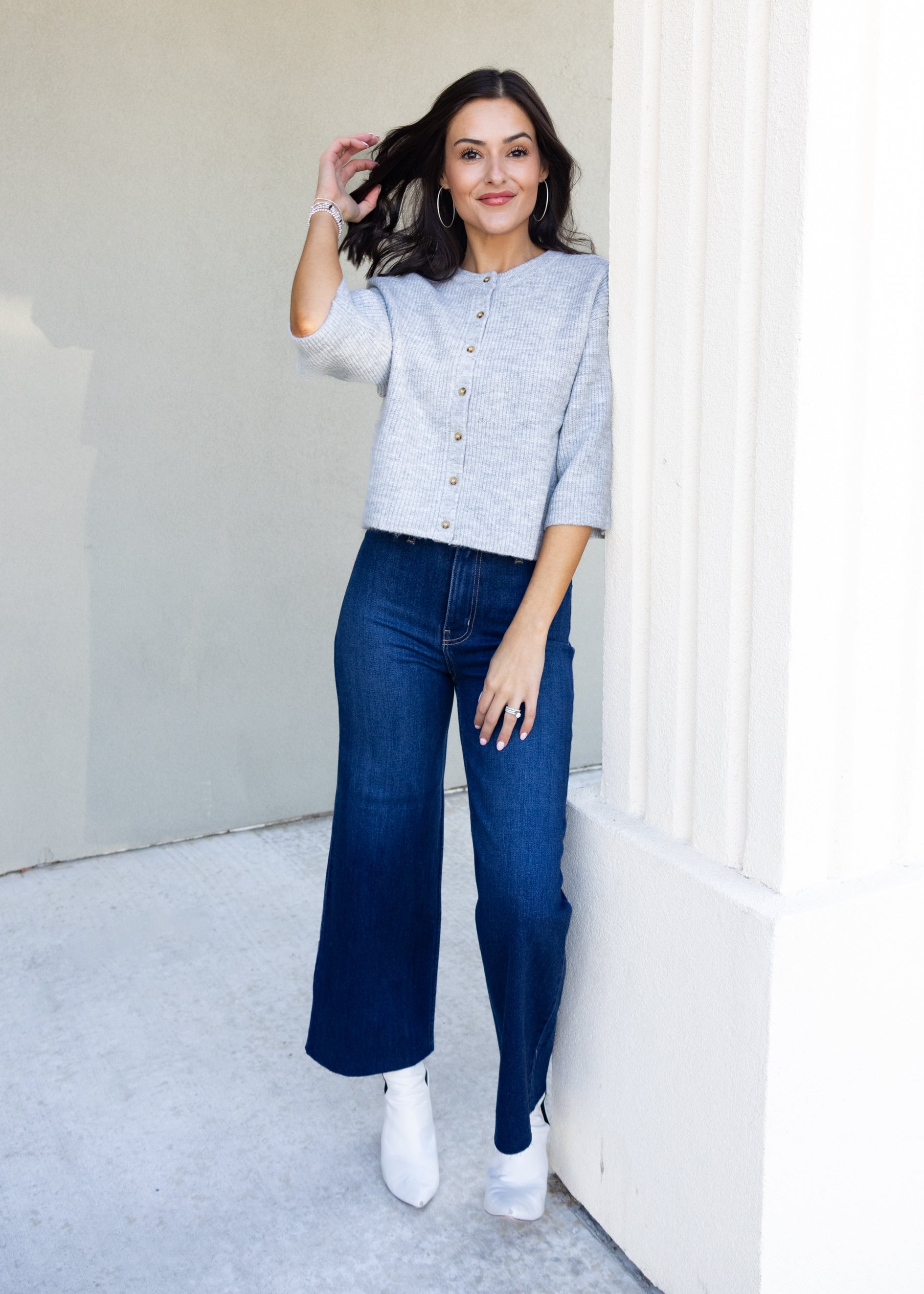 Woman wearing a light grey cardigan and dark blue jeans outdoors.