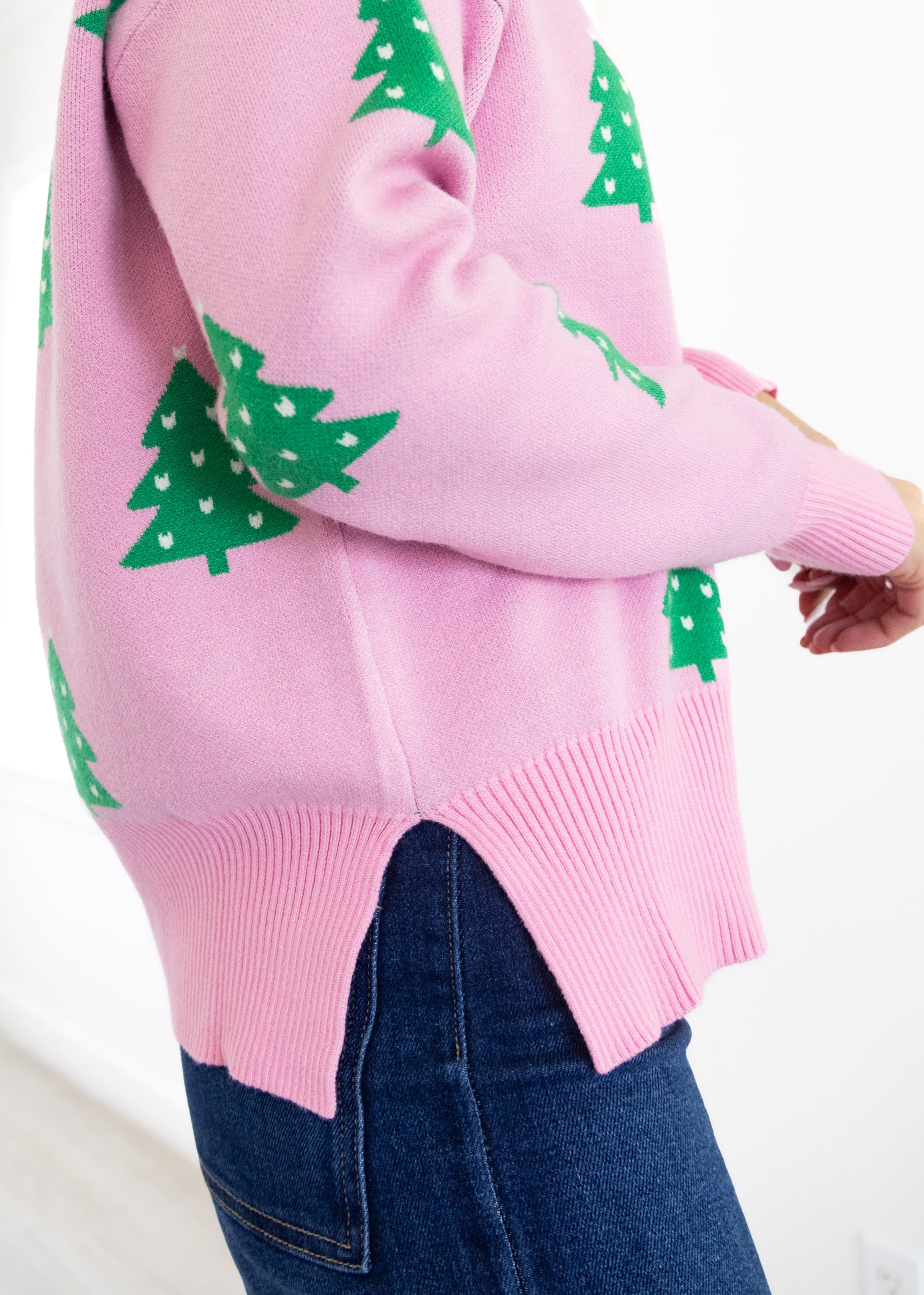Pink sweater with green tree patterns worn by a person on a white background